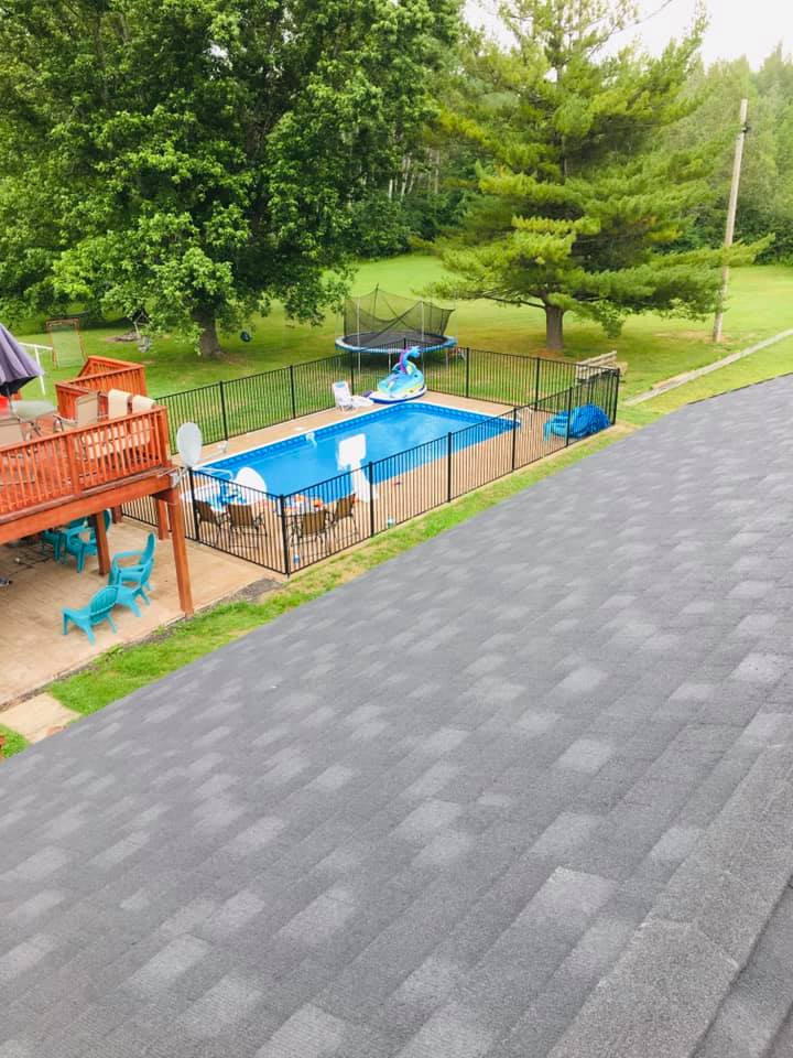 Backyard with a small blue pool, trampoline, wooden deck, and gray shingled roof in the foreground