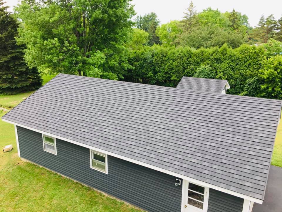 Aerial view of a gray-shingled house with green siding surrounded by trees and lawn