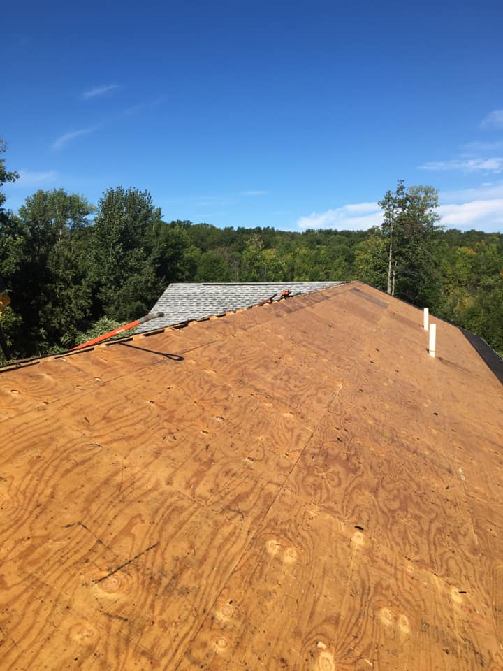 Partially covered roof under construction with plywood sheathing and a blue sky overhead