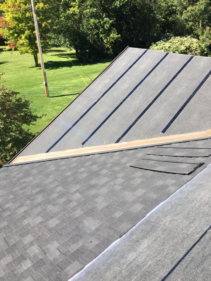 Roof with dark shingles and black metal panels, viewed from above near a grassy yard.