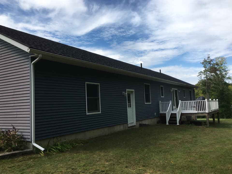 Single-story blue house with white trim and a small raised deck on a grassy lawn.