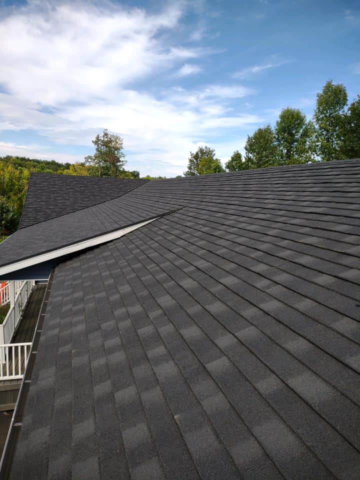 Dark gray shingled roof with a sloping peak under a partly cloudy sky, trees in the background