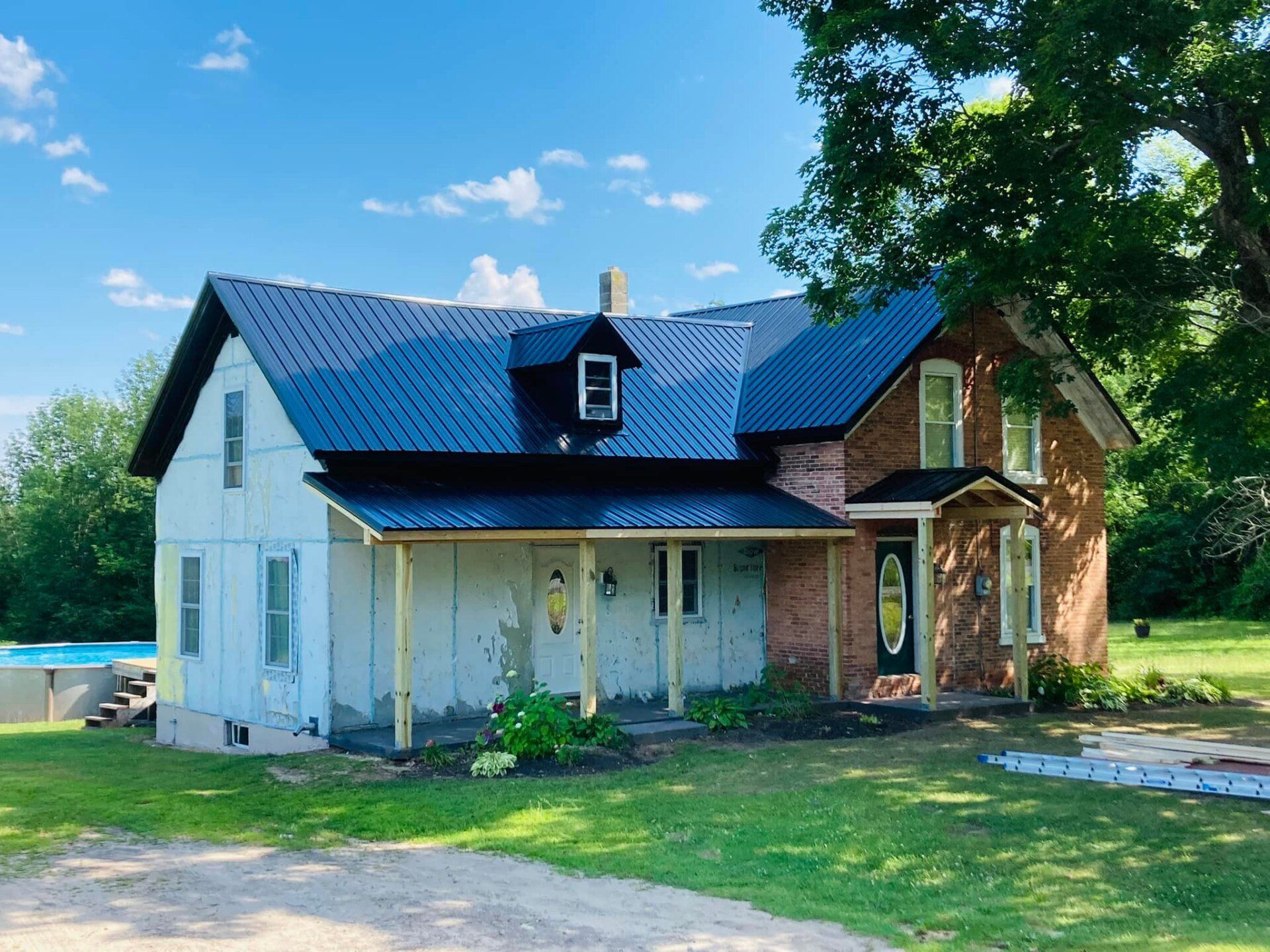 White house with blue roof and porch beside a brick section, set in a sunny grassy yard.