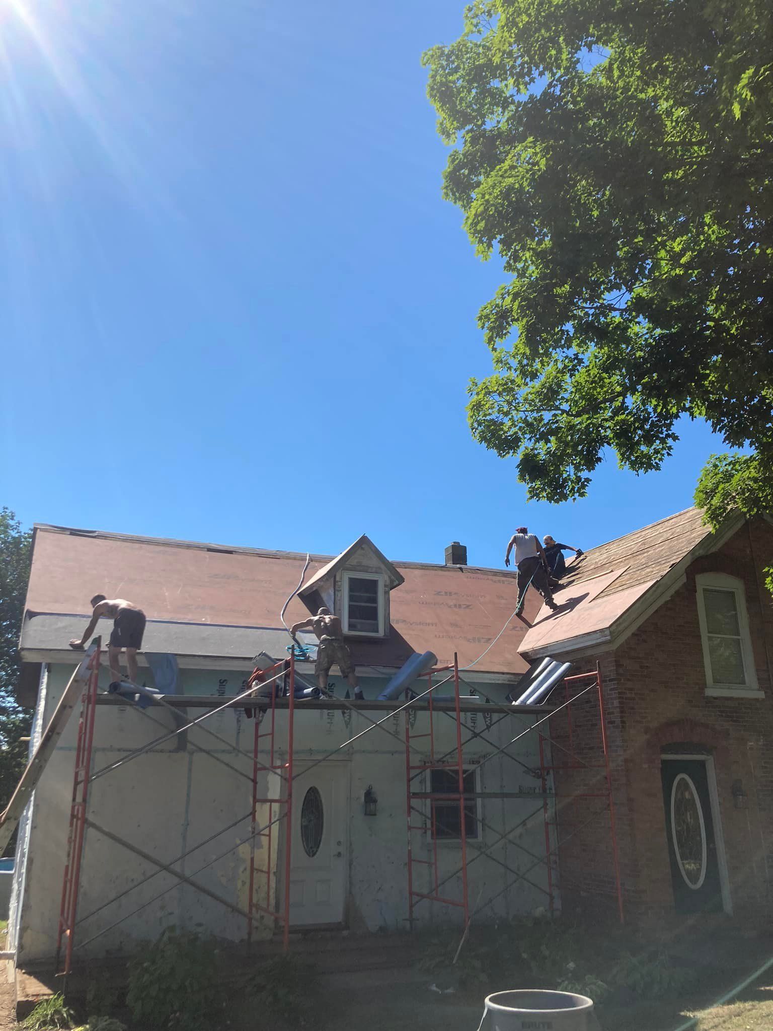 Scaffolding in front of a white house with a red roof under a bright blue sky and tree branches