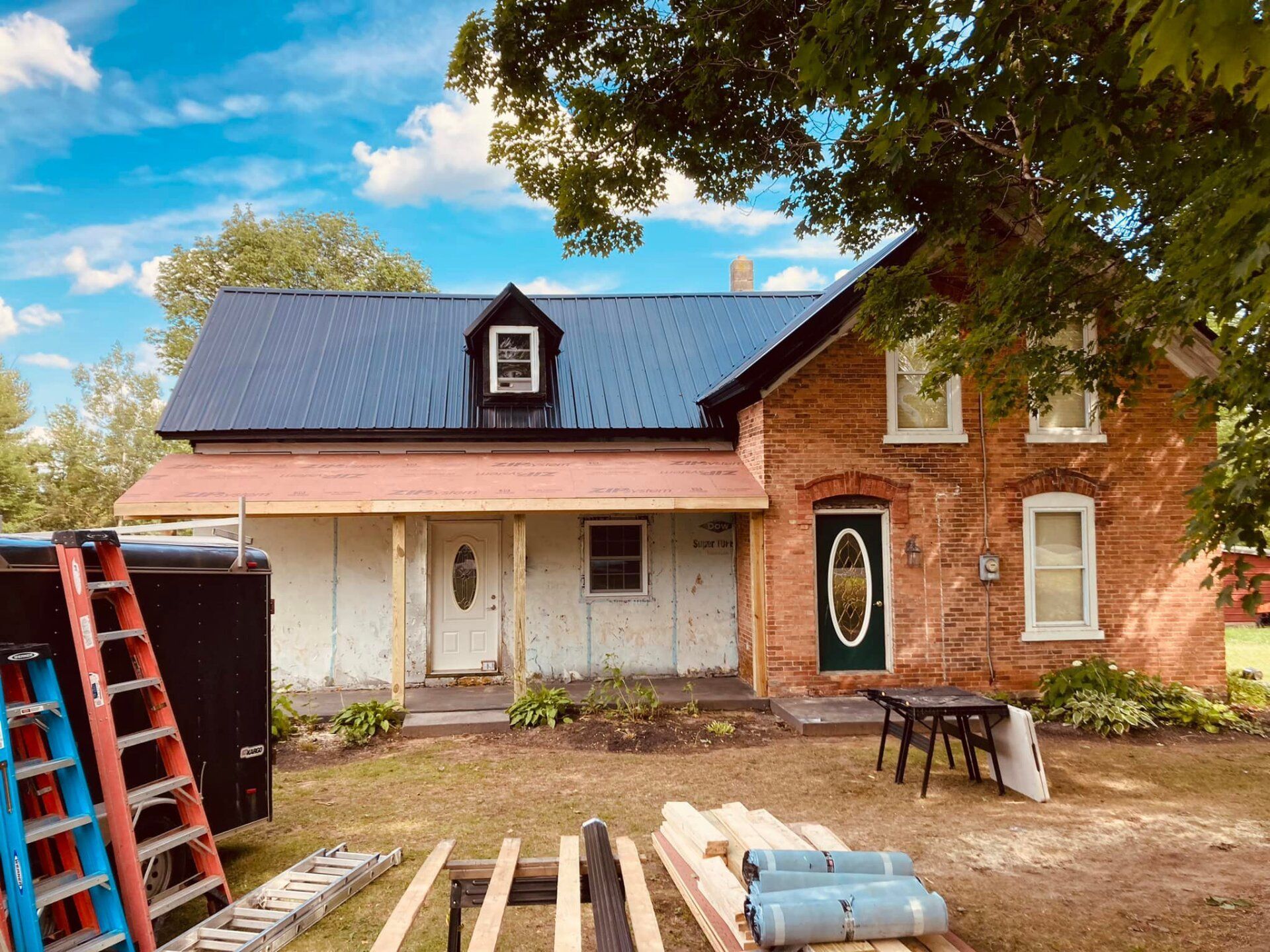 Partially renovated brick and white house with ladder, tools, and construction materials in the yard