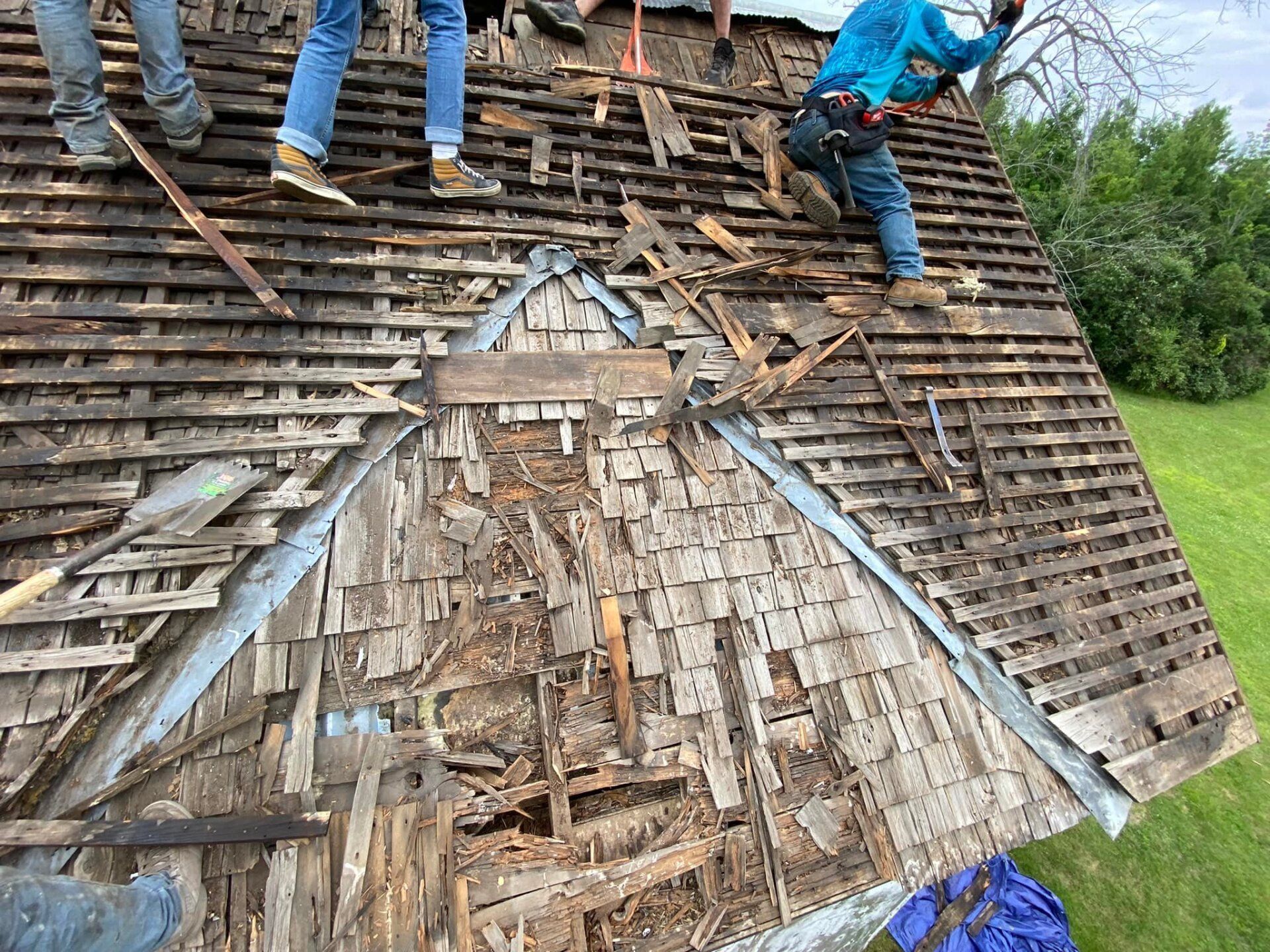Workers repairing a damaged shingled roof with exposed wood and missing tiles