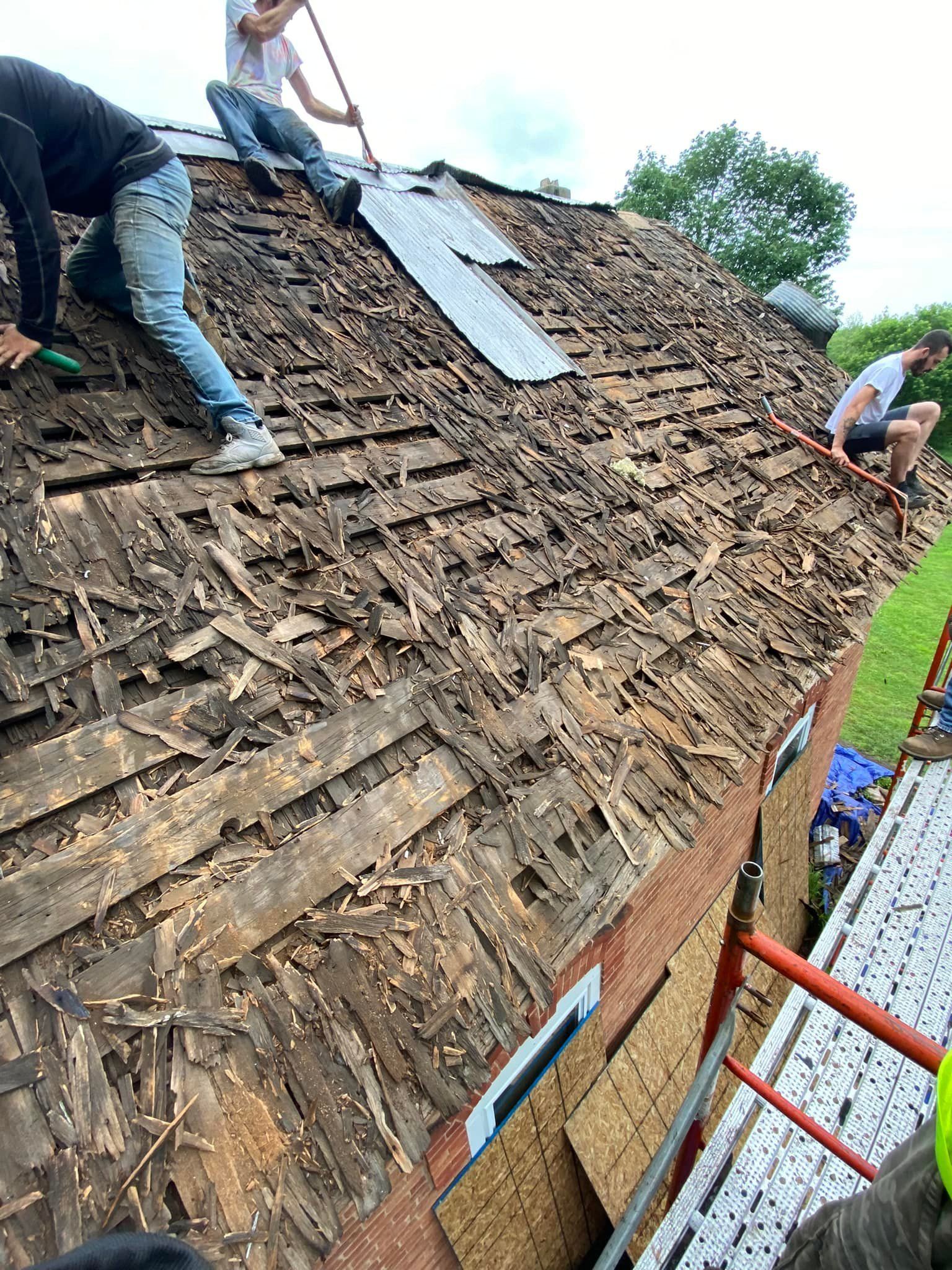 Workers repairing a steep, weathered shingle roof with ladders and tools.