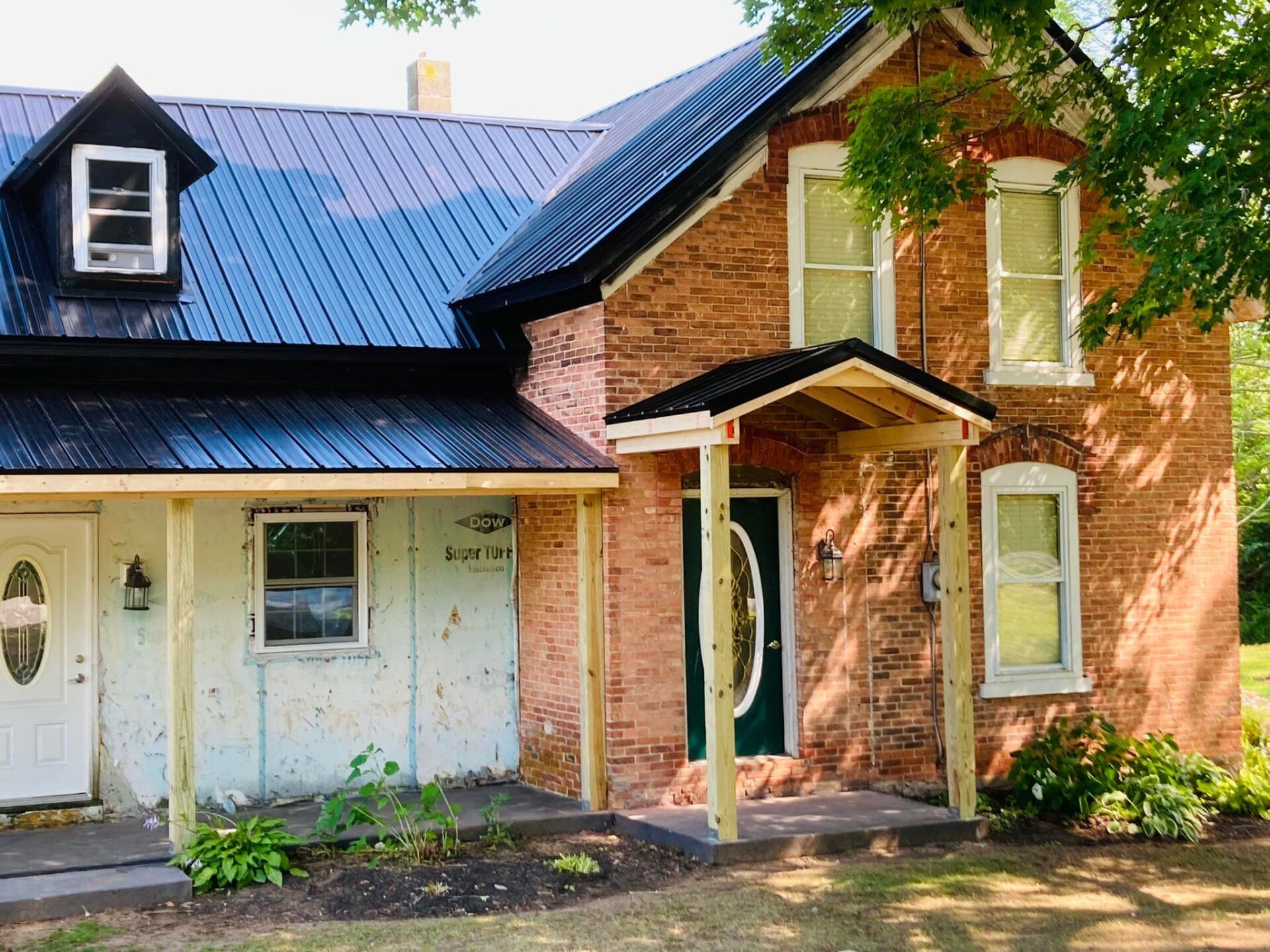Two-story brick house with blue metal roof and white porch trim, seen from the front
