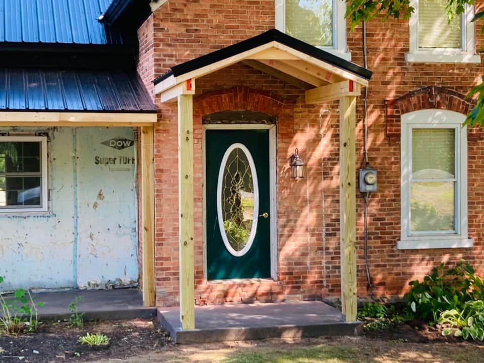 Brick house entrance with green front door, oval glass panel, and small covered porch