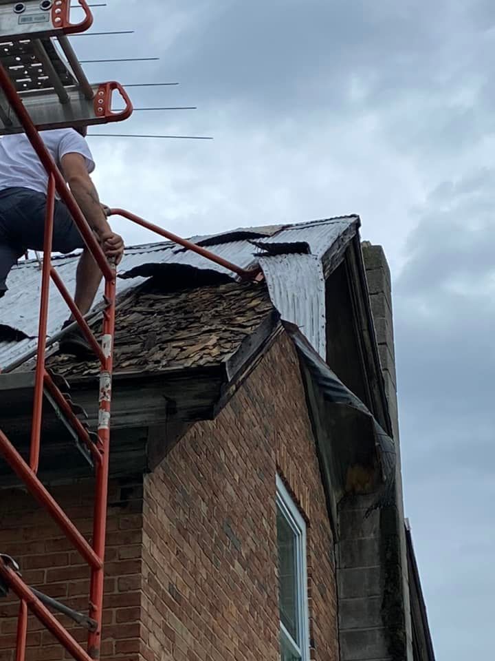 Damaged brick building with a partially collapsed roof and red scaffolding against a cloudy sky