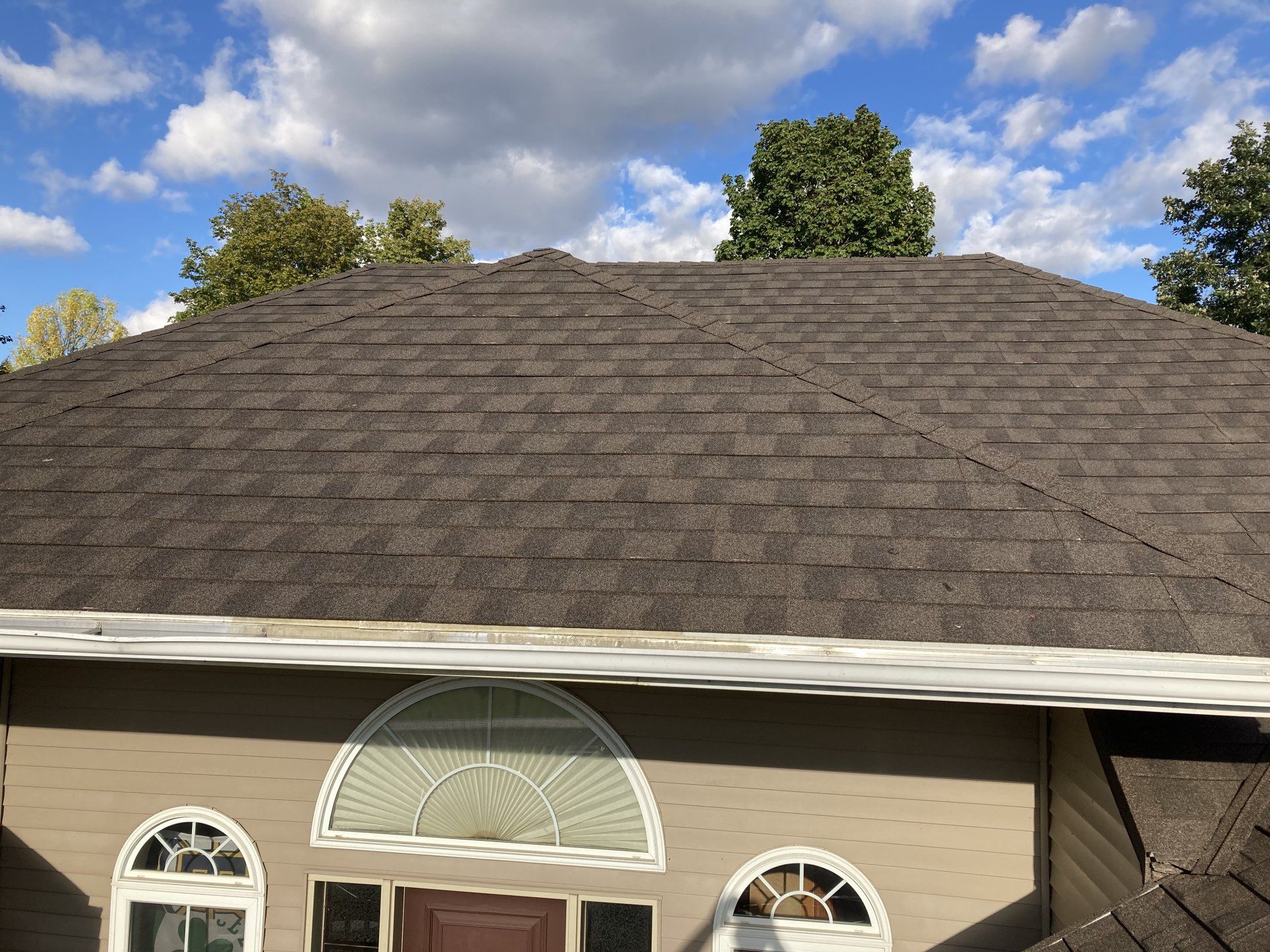 Gray shingle roof on a house under a partly cloudy blue sky