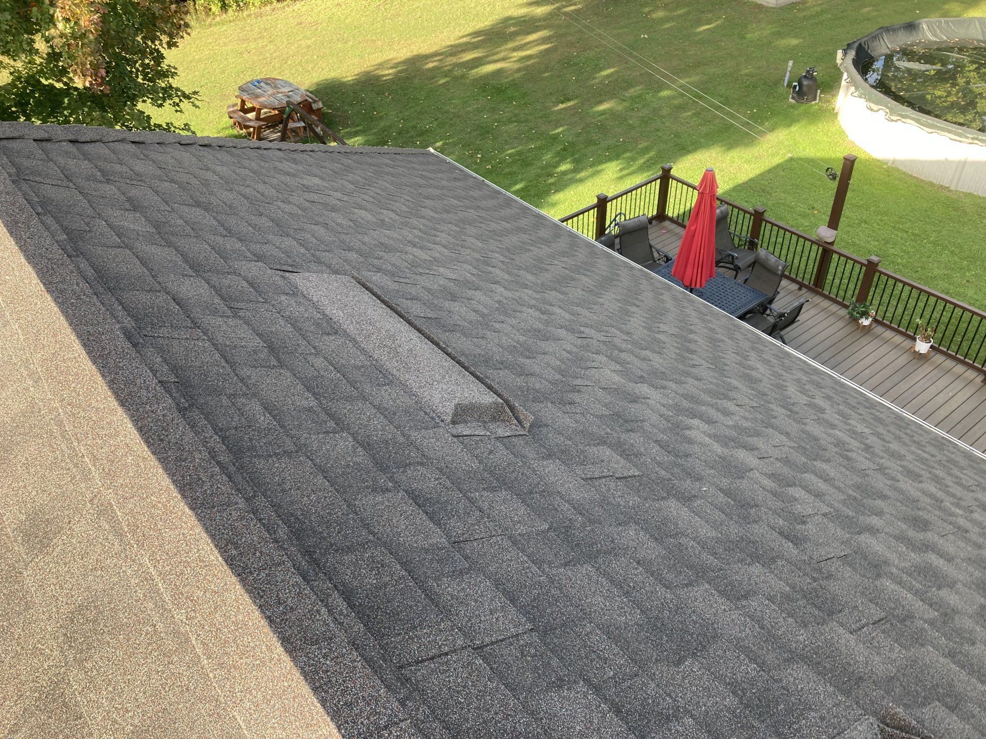 Weathered gray shingled roof overlooking a backyard patio with red umbrella and green lawn