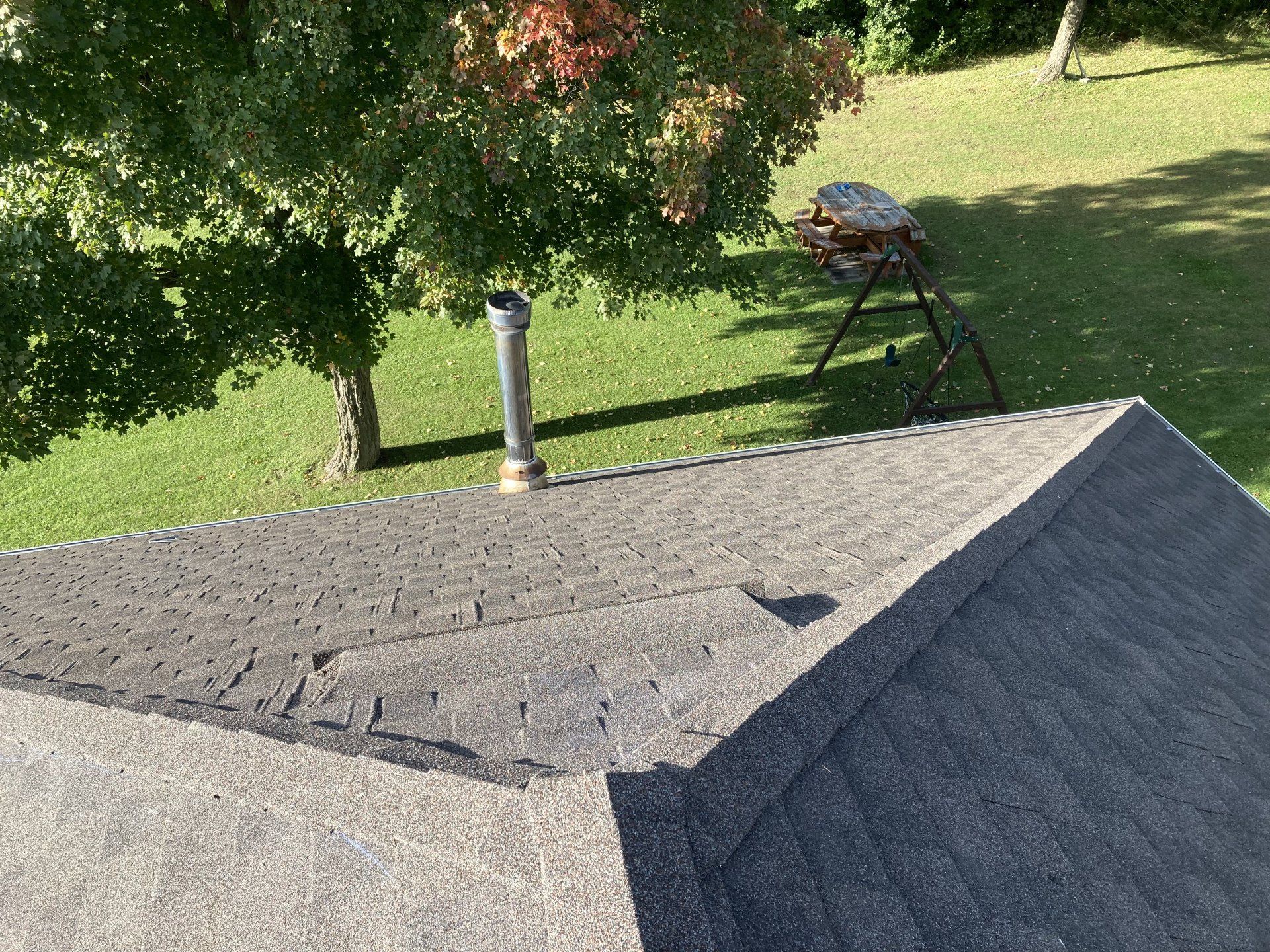 Shingled rooftop with vent pipe, overlooking a grassy yard with a tree and charcoal grill