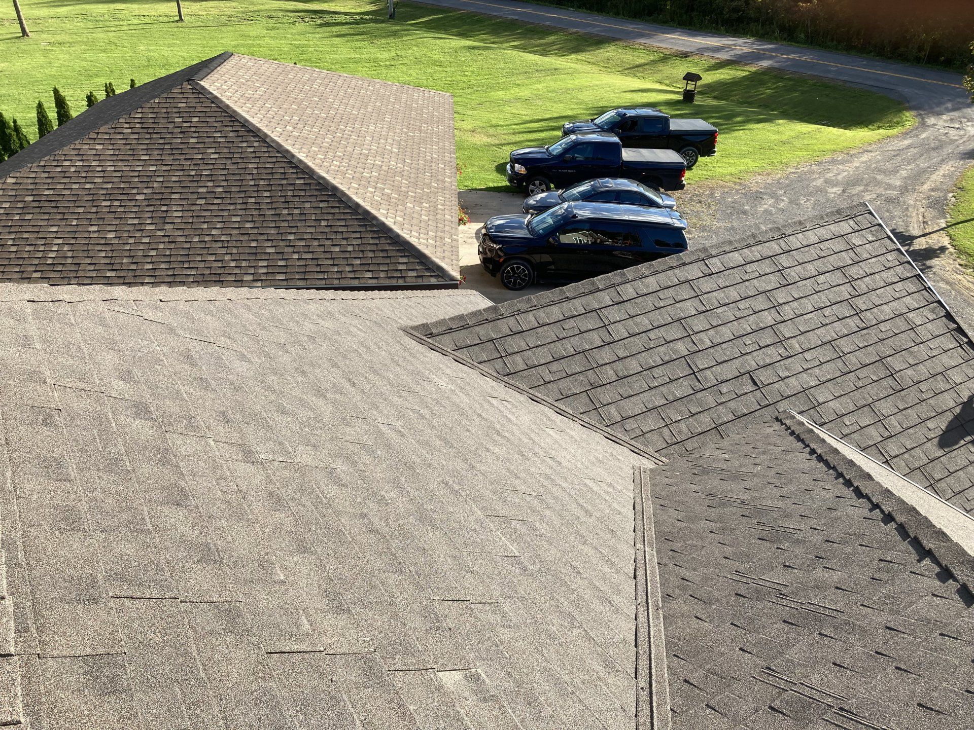 Rooftops of a house with parked cars and a grassy yard in the background