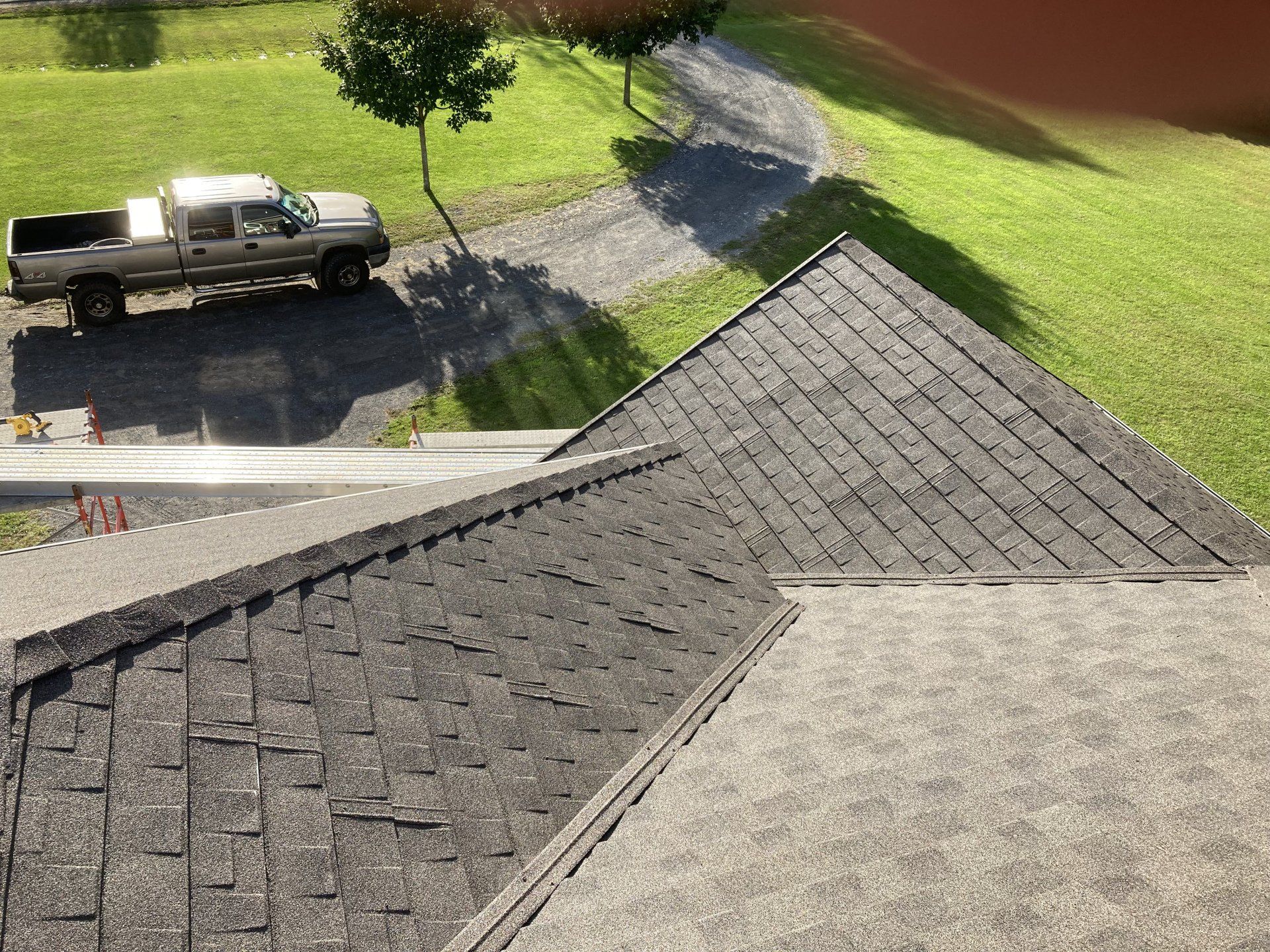 Roof with gray shingles in foreground, with a pickup truck and driveway beside a green lawn.