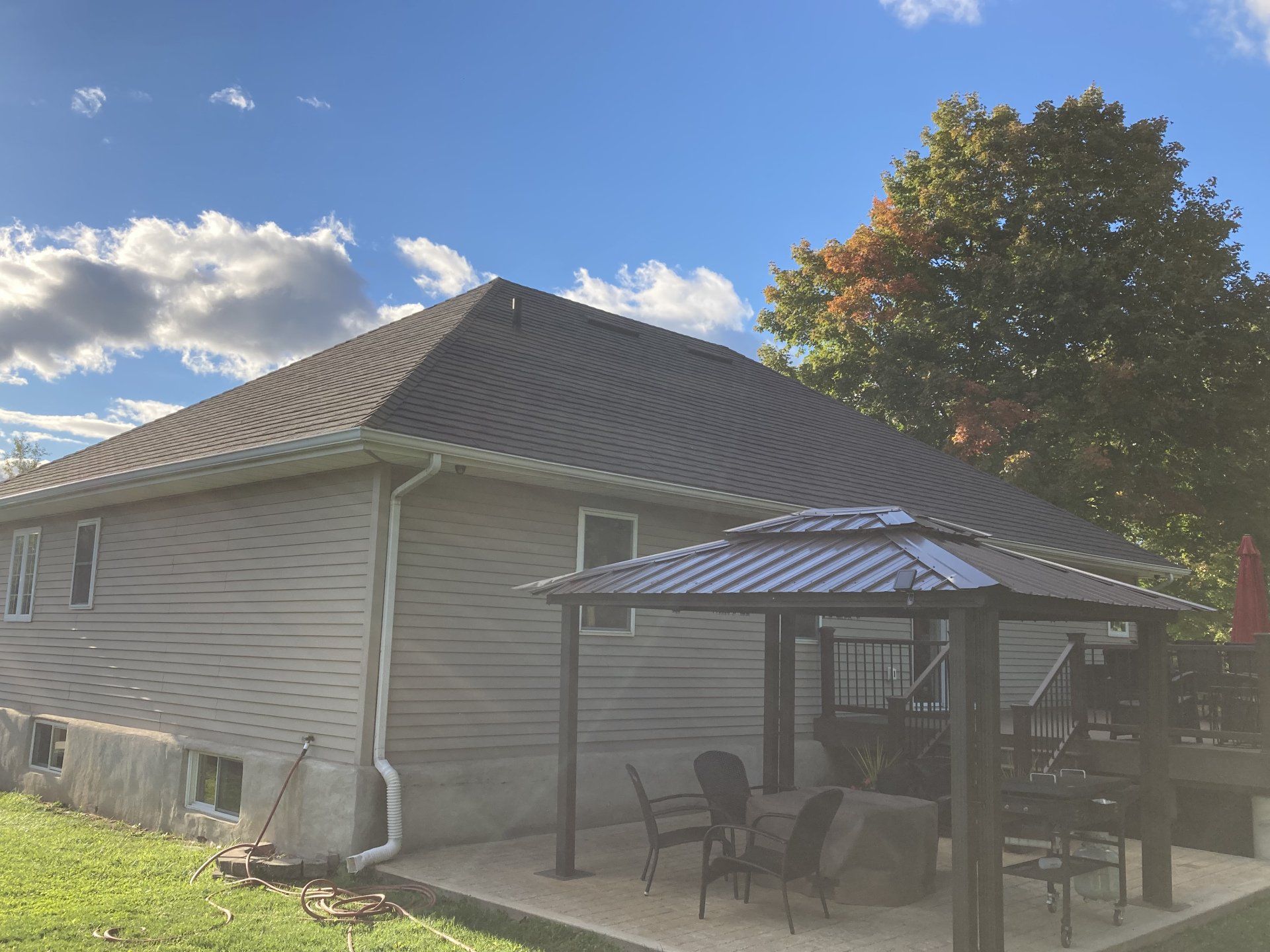 Suburban house with gray siding, dark roof, and a patio with chairs under a striped canopy