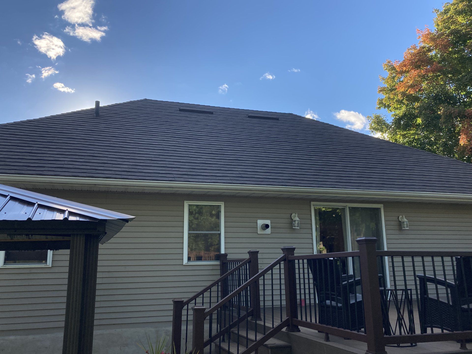 House roof with wavy dark shingles, front porch railing, and blue sky with clouds above.