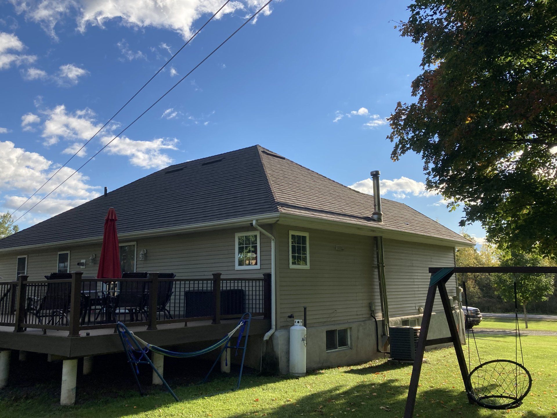 Backyard view of a house with a deck, patio table, red umbrella, and swing set under a blue sky
