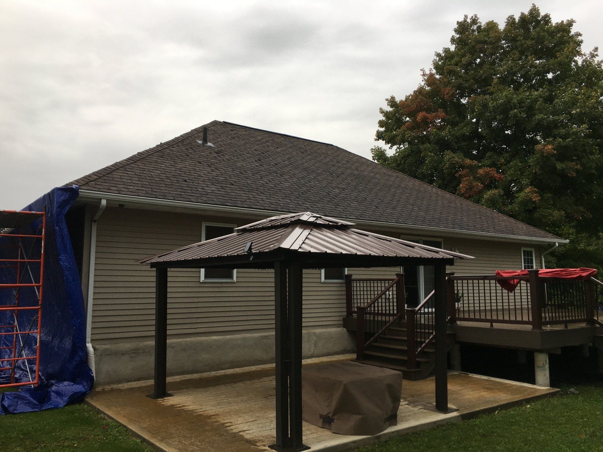 Backyard patio with a gazebo, deck, and a house with gray siding and a shingled roof