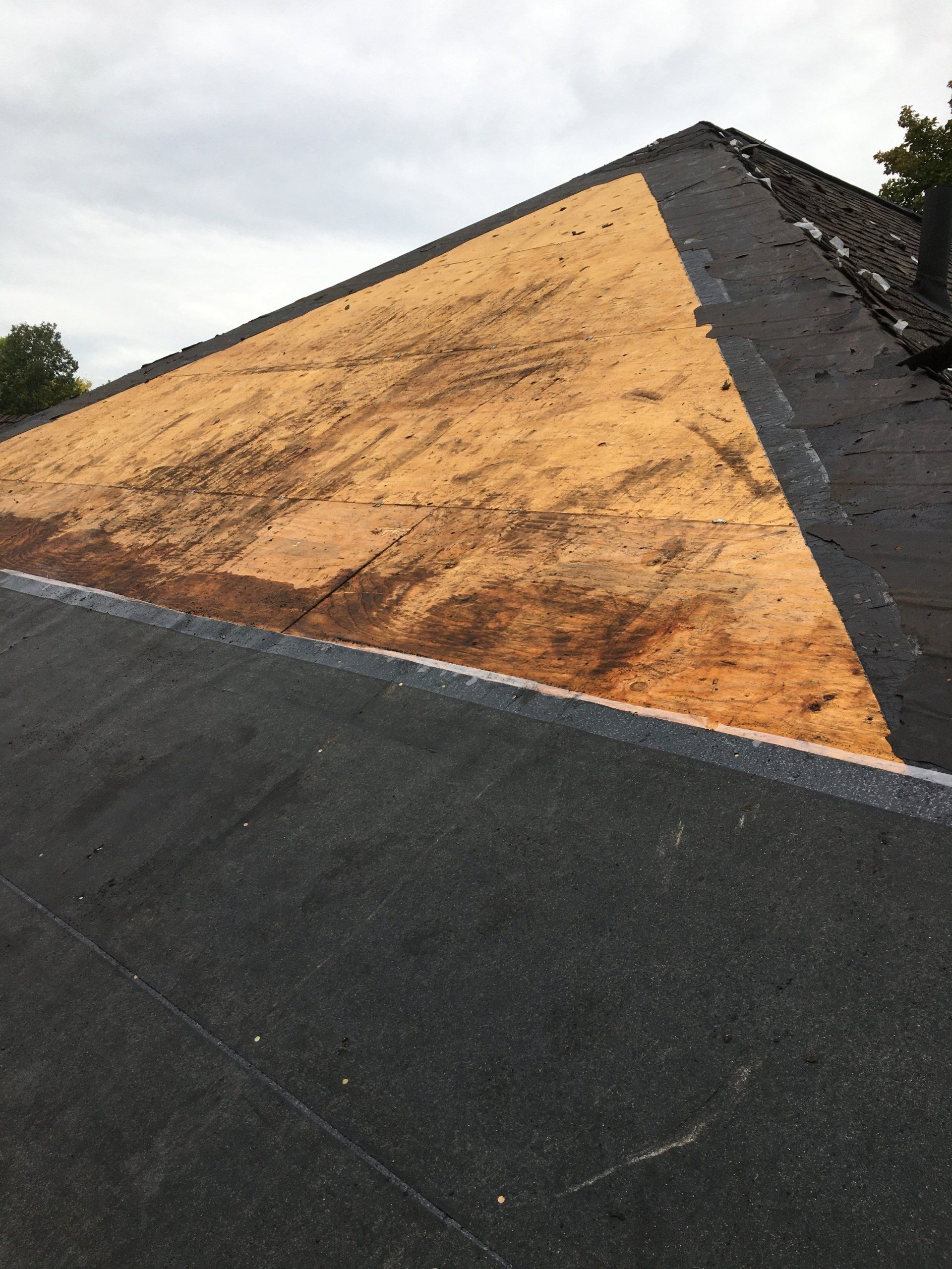 Roof under repair with a large plywood section and black roofing material around it