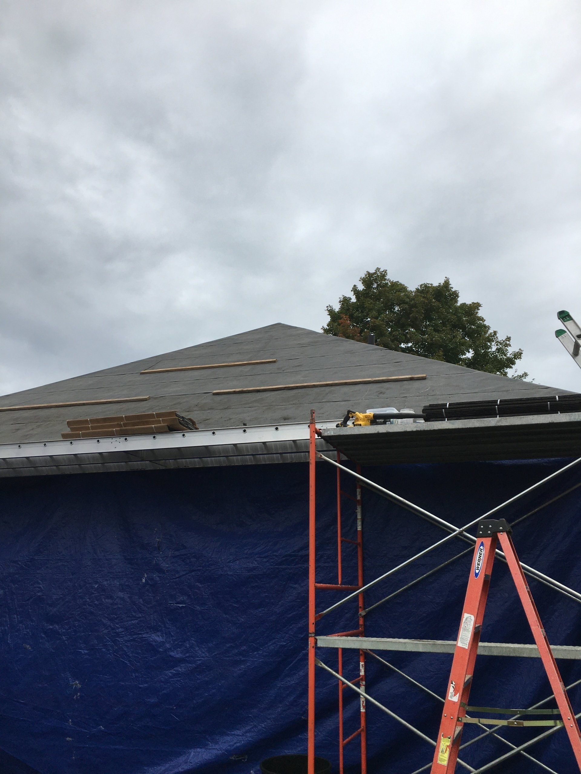 Roof under repair with blue tarp, red scaffolding, and cloudy sky
