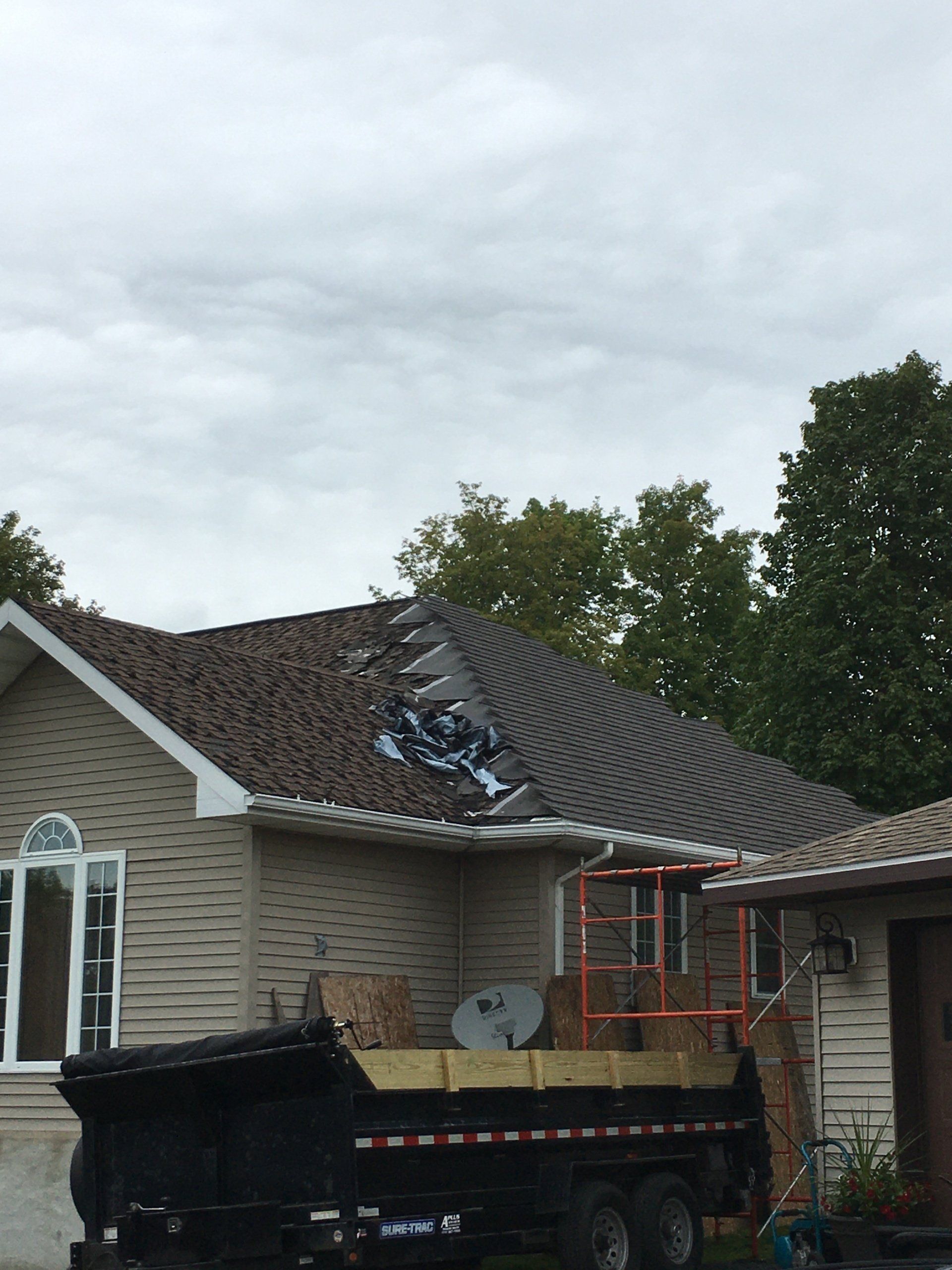 Workers repair storm-damaged roof on a house beside a truck and ladder under cloudy skies