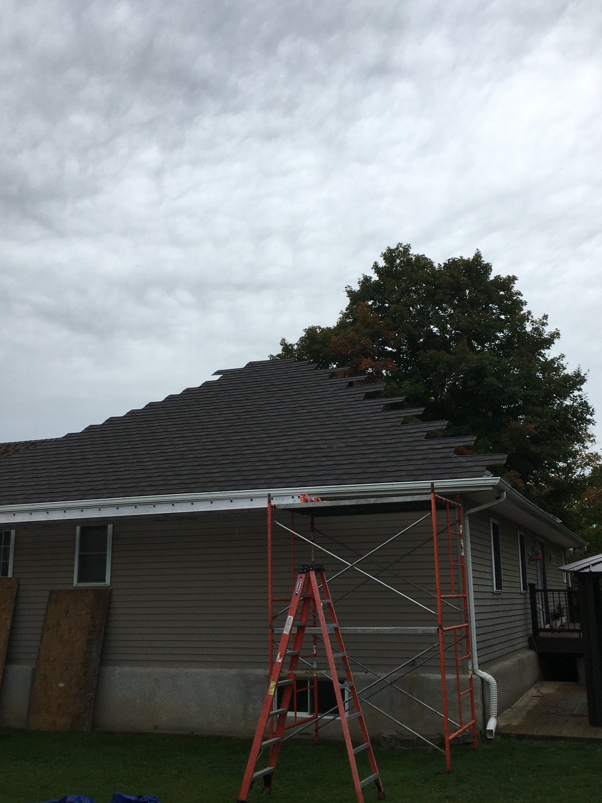 House roof under repair with red ladder and scaffolding in front of gray siding