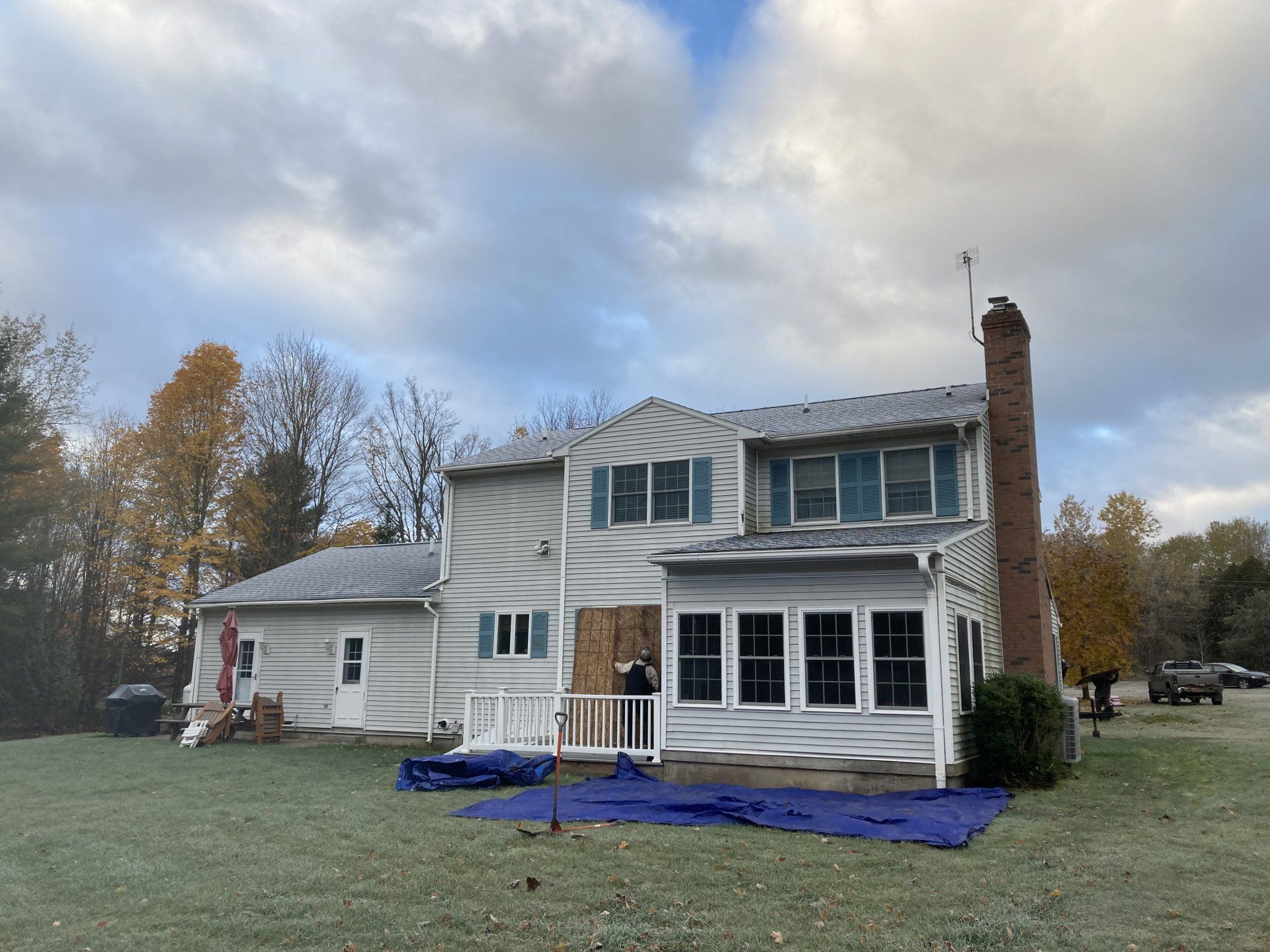 Two-story white house with blue tarps and ladders, under exterior renovation on a cloudy day
