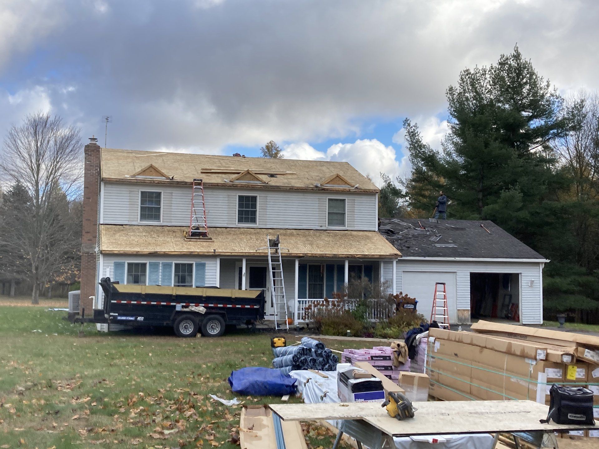 Two-story house under renovation with dumpster, lumber piles, and overcast sky