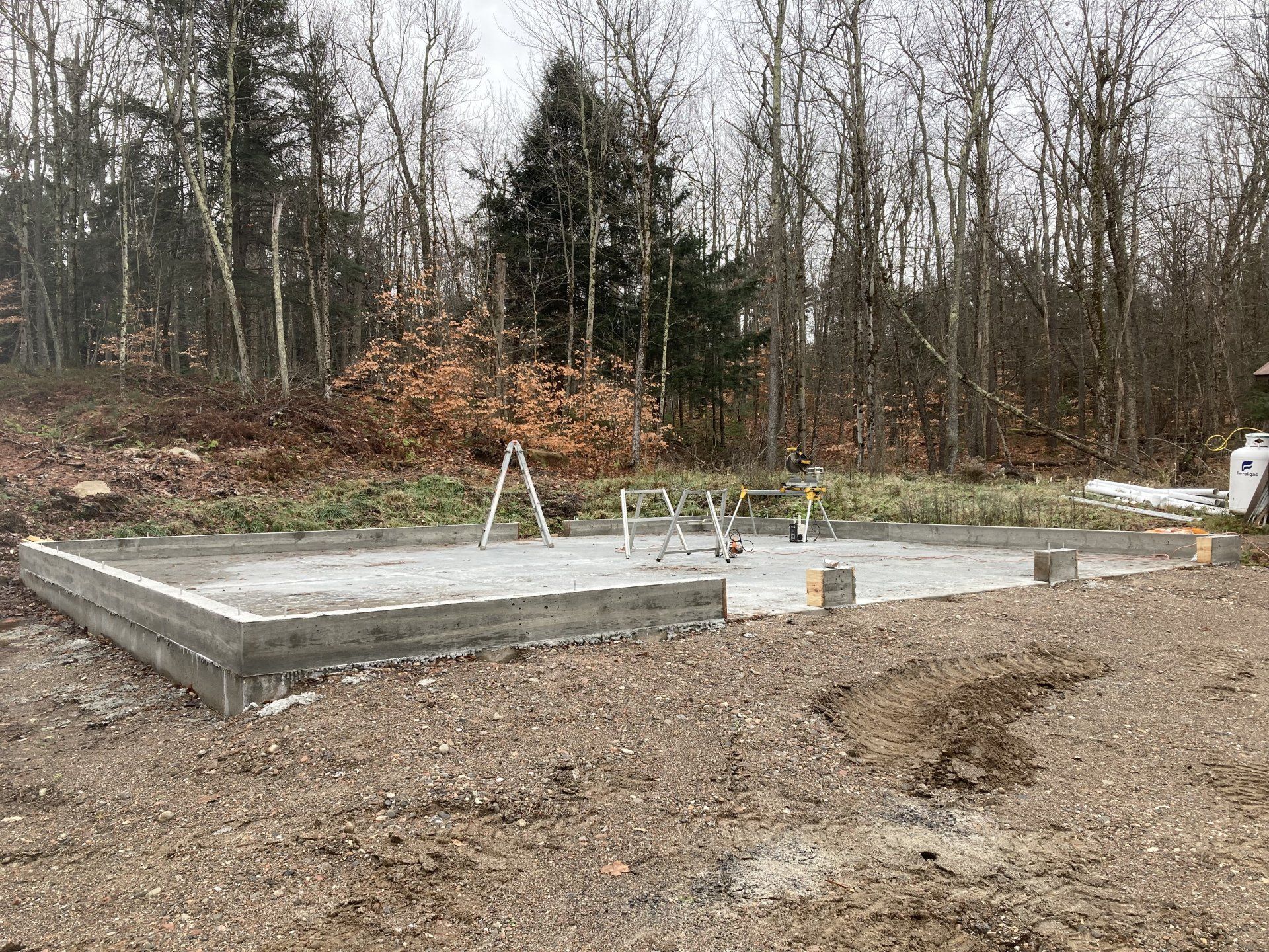 Concrete foundation slab under construction in a wooded lot with an A-frame ladder nearby