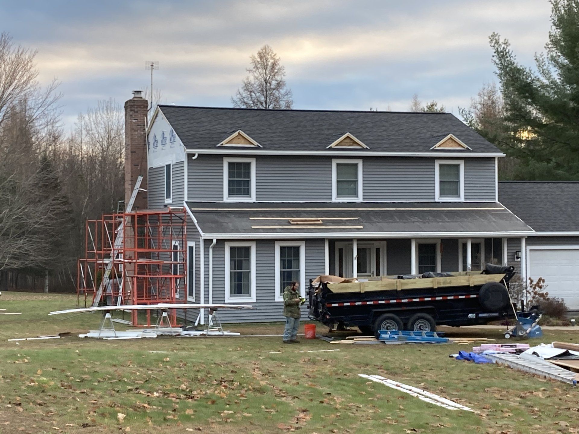Two-story gray house with scaffolding and a work trailer in the front yard