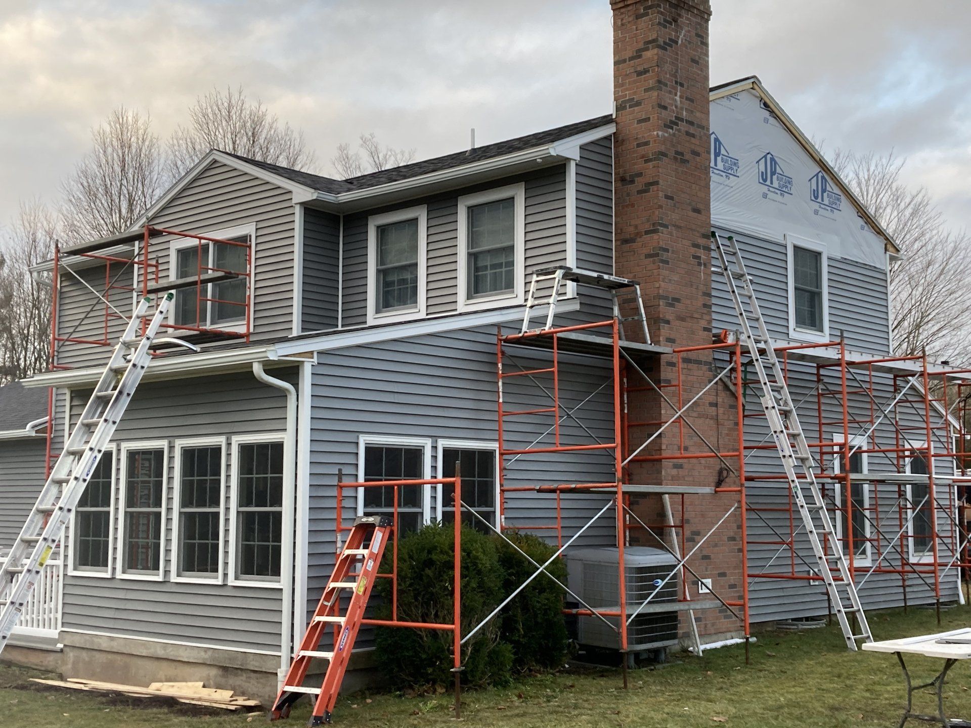 Two-story gray house with scaffolding and ladders during exterior renovation
