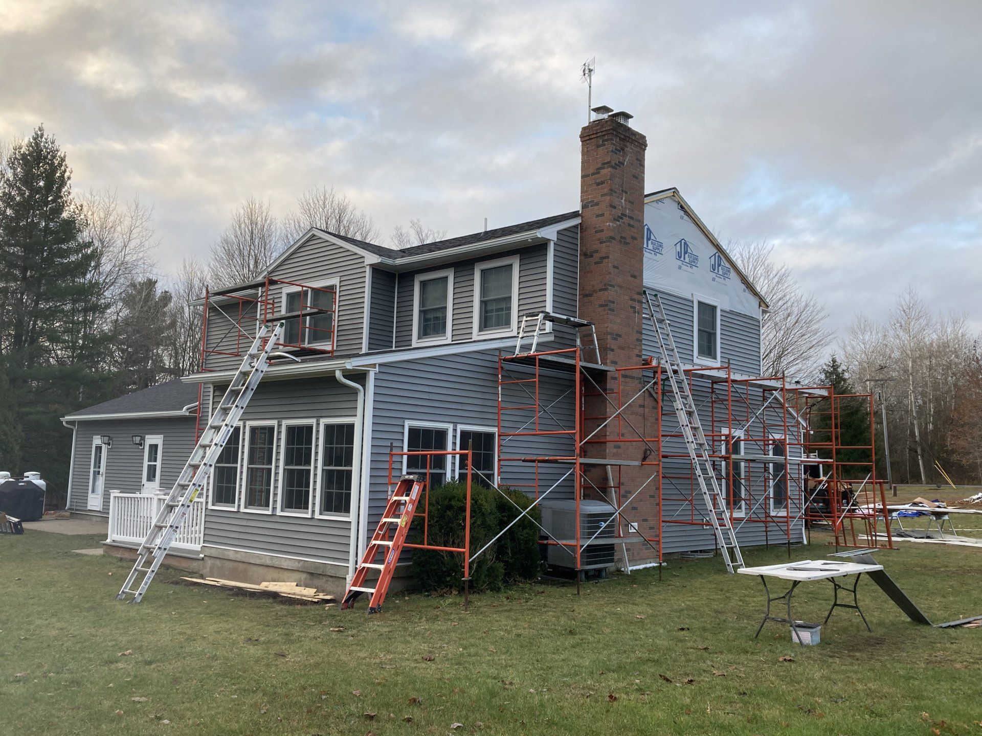 Gray two-story house with scaffolding and ladders during exterior renovation