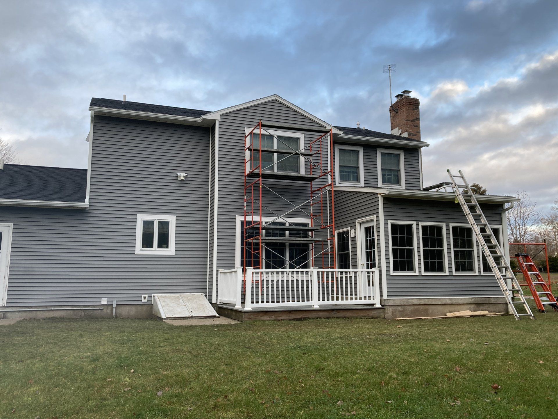 Gray two-story house with scaffolding and ladders during exterior renovation