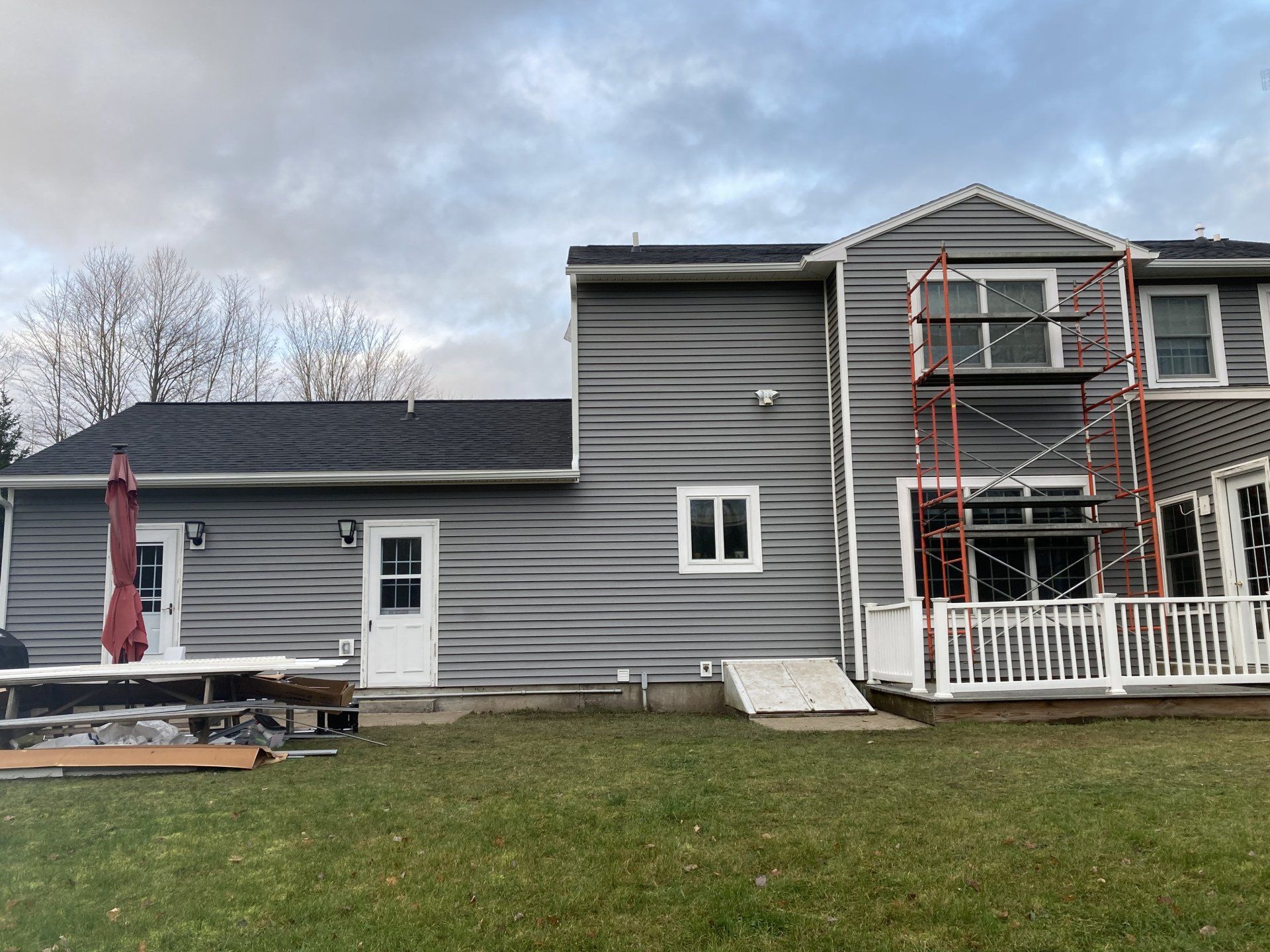 Gray two-story house with white trim, a small porch, and scaffolding on the front under a cloudy sky