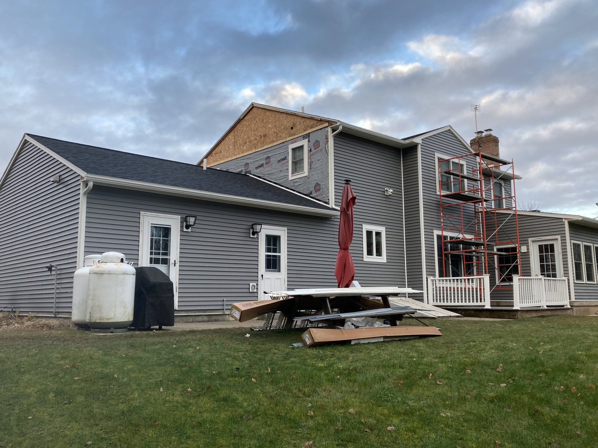 Gray house with deck and patio furniture in a grassy yard under a cloudy sky