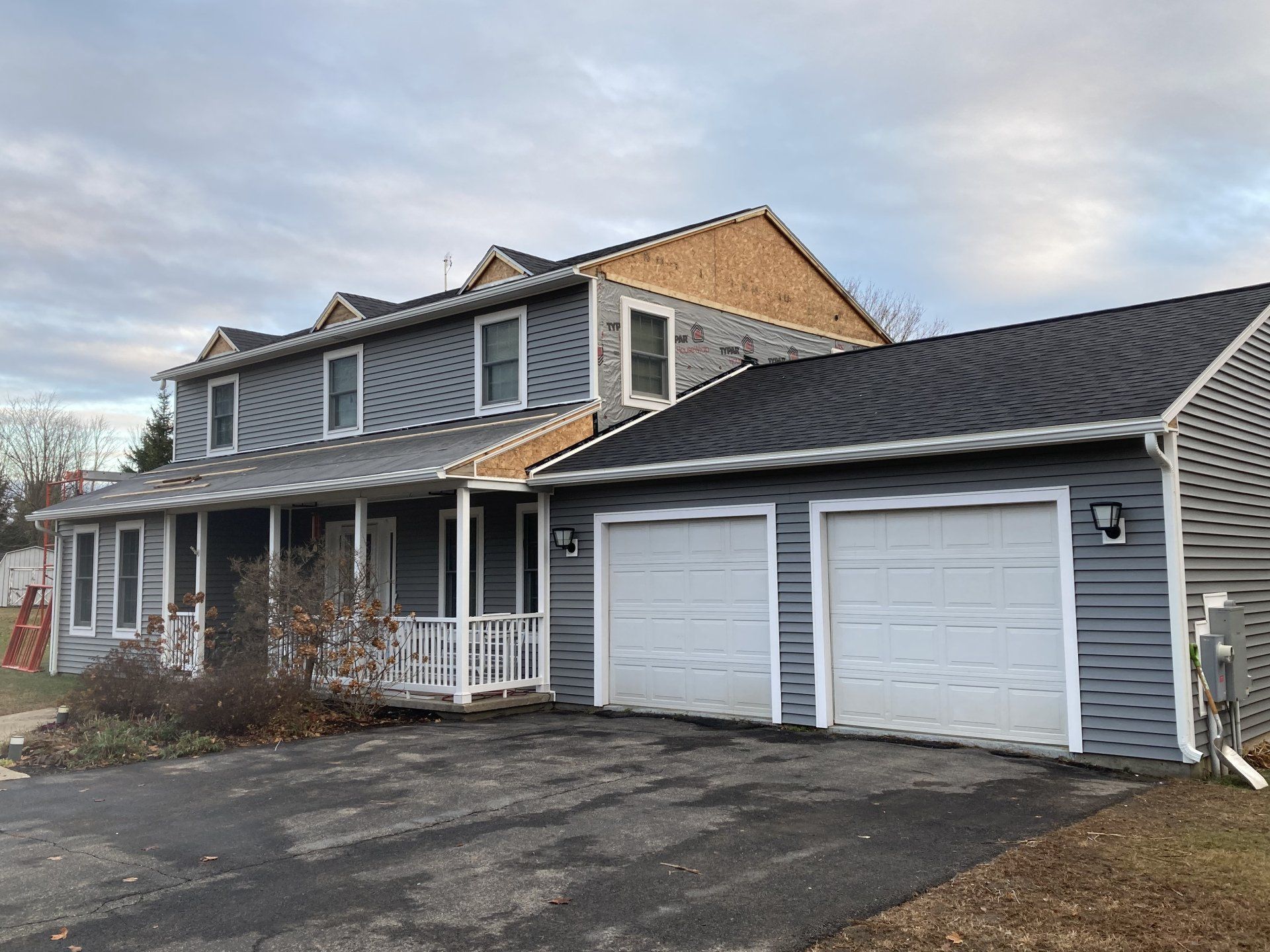 Two-story gray house with attached double garage and driveway under a cloudy sky