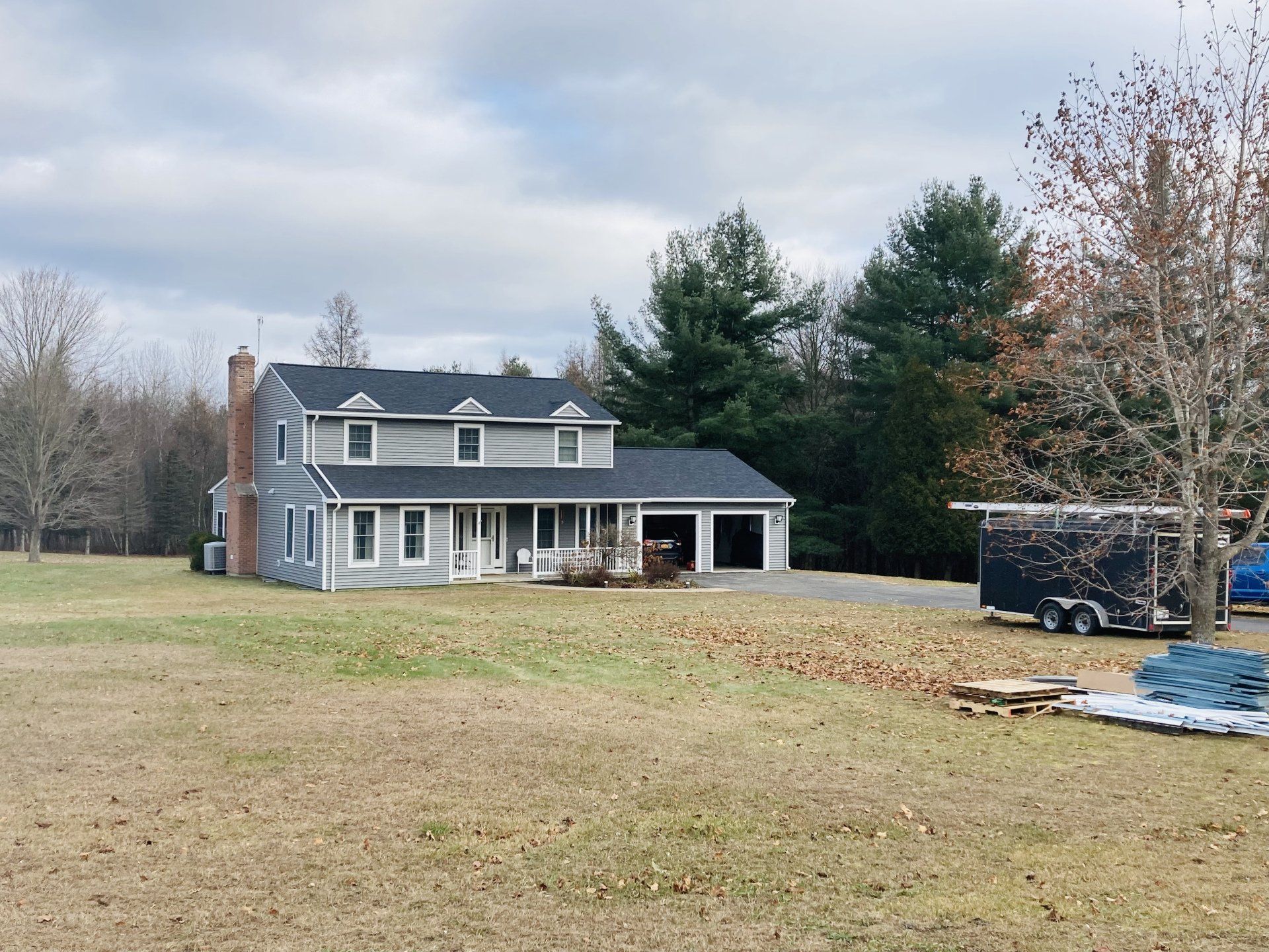 Two-story gray house with white trim and porch in a large grassy yard under a cloudy sky