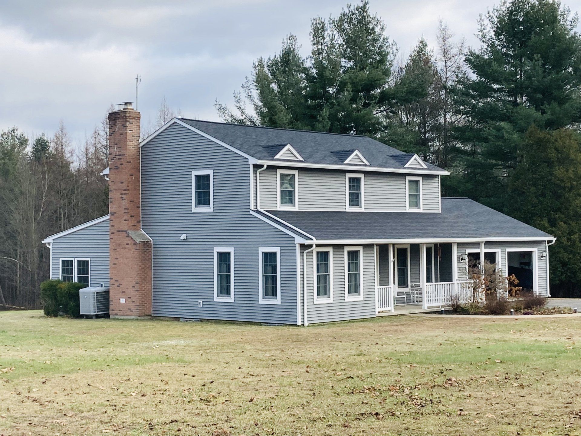 Gray two-story house with brick chimney, white porch, and dormer windows on a grassy lot