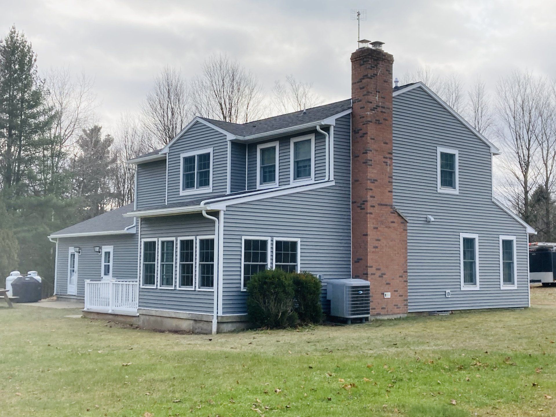 Gray two-story house with brick chimney and attached garage on a grassy lawn