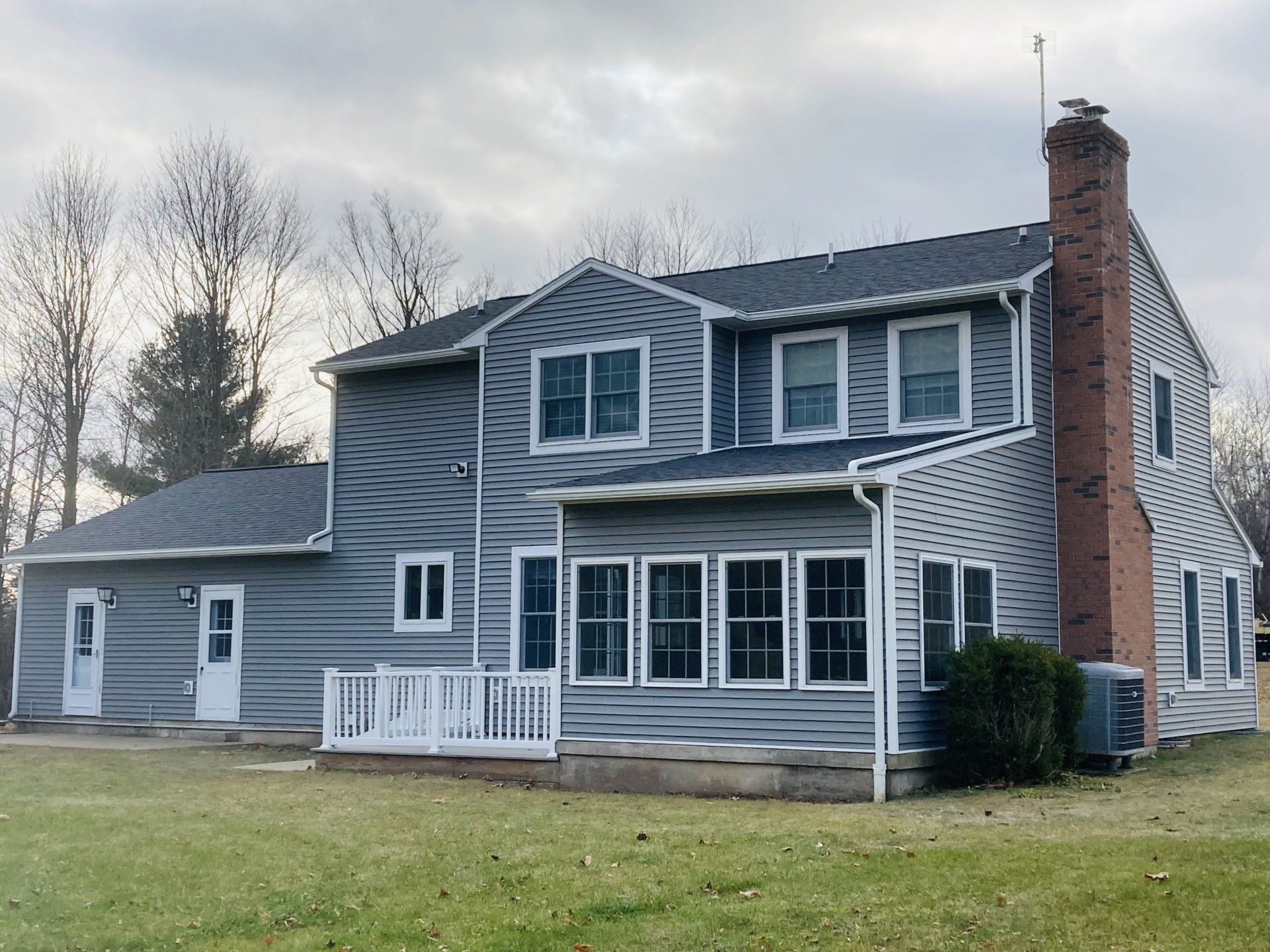 Two-story gray house with white trim, covered front porch, and a brick chimney on a grassy lawn.