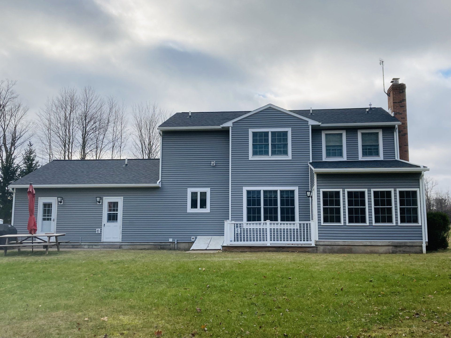 Gray two-story house with white trim and porch in a grassy yard under a cloudy sky