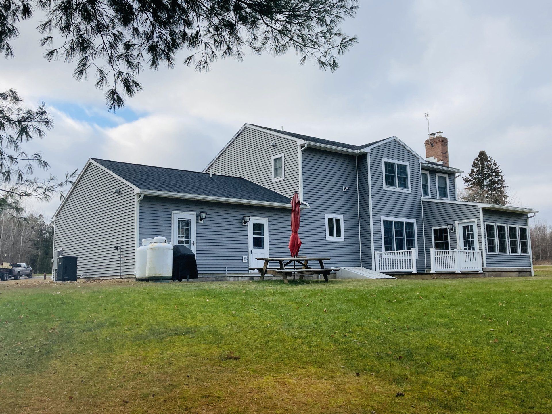 Gray house with striped siding and a red flag on a grassy lawn under an overcast sky