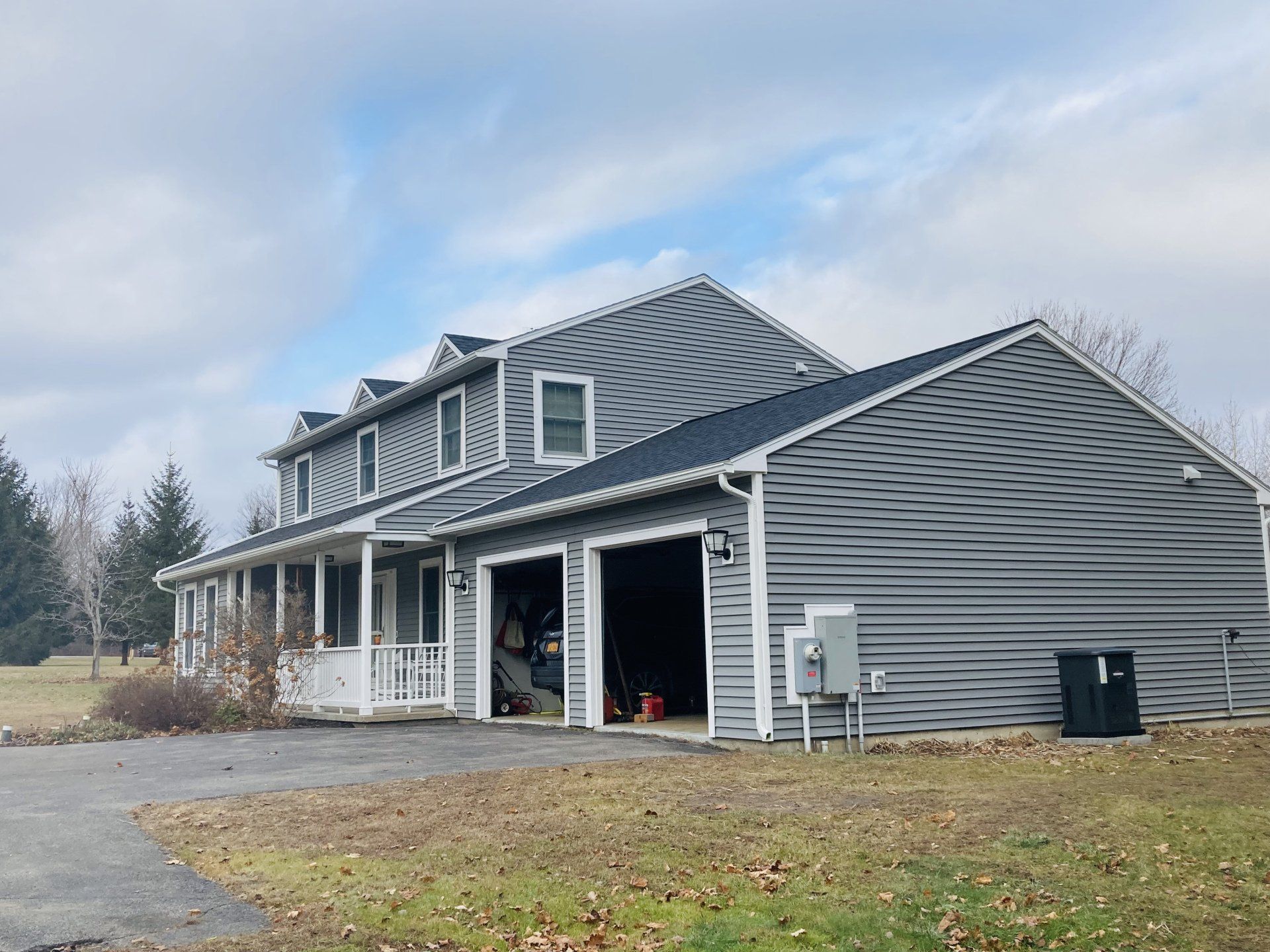 Gray house with a covered porch and dormer windows on a grassy lot under a cloudy sky