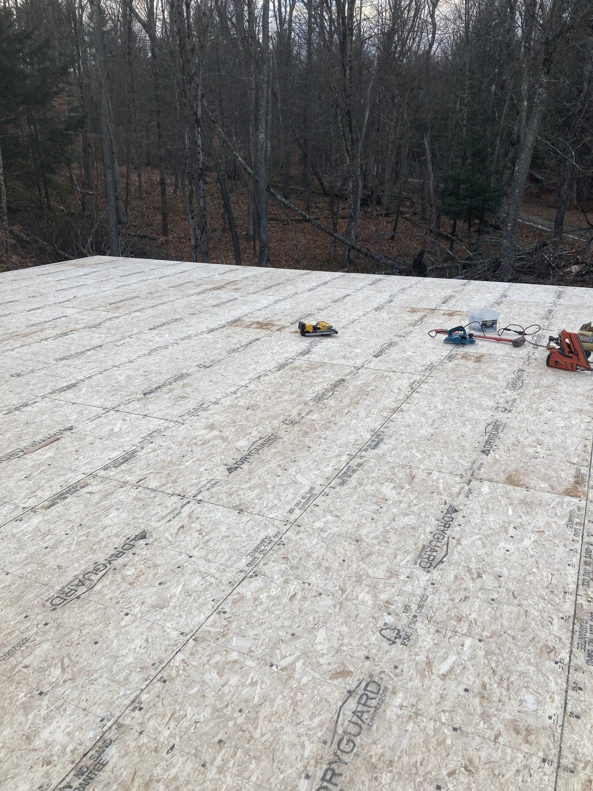 Snow-covered rooftop with scattered tools near a wooded tree line