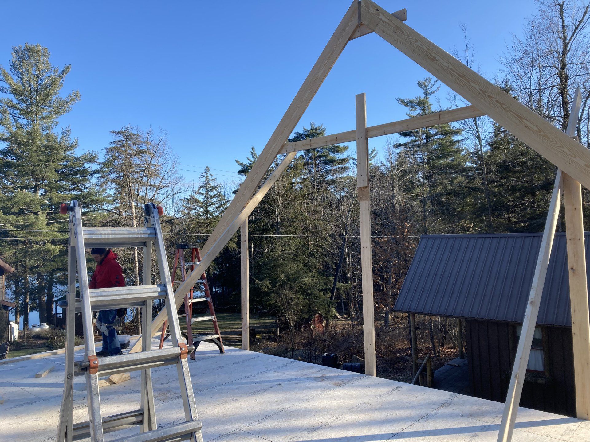 Wooden playground structure under construction with ladders and a climbing frame in a snowy yard