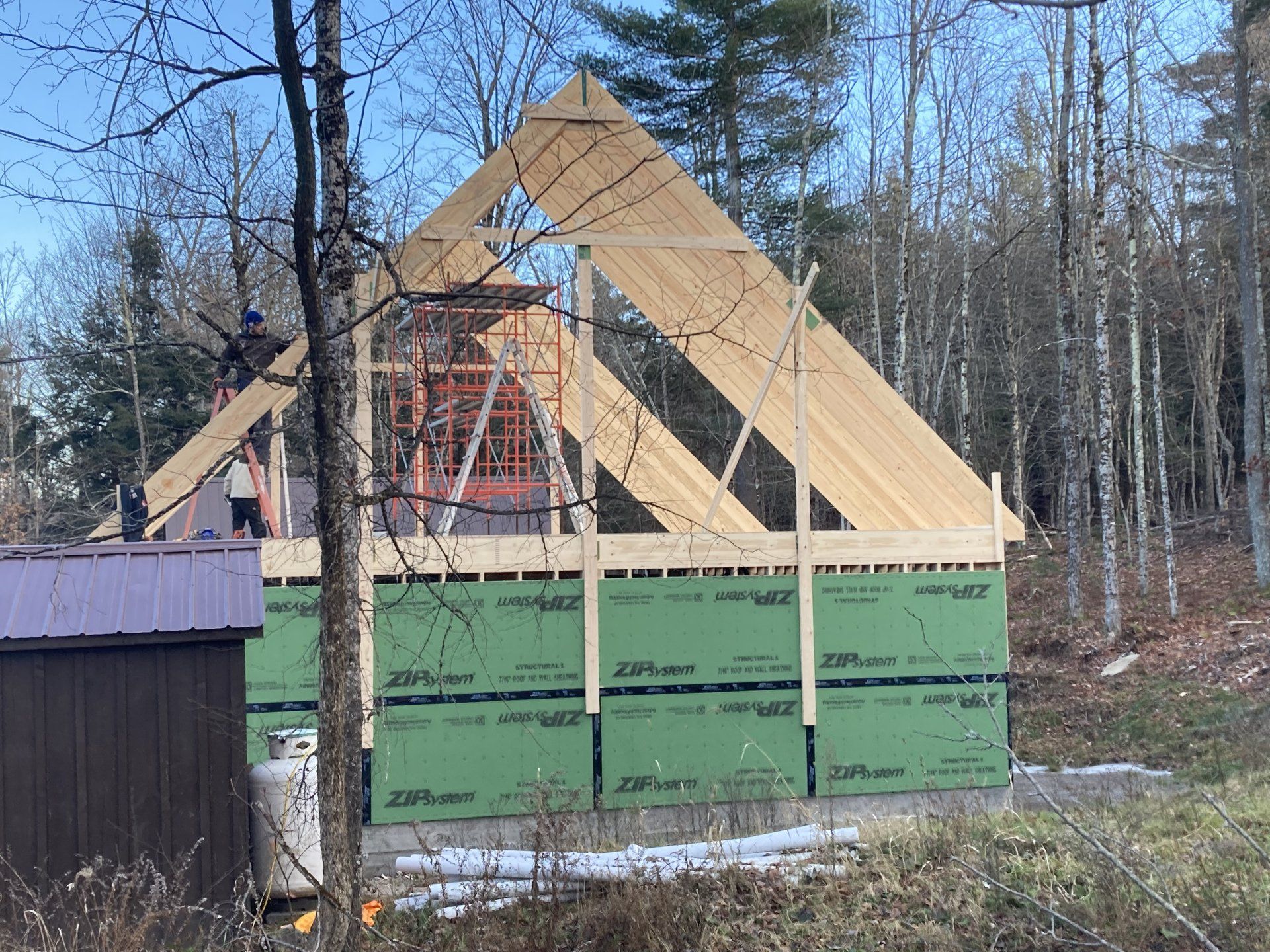 Partially built A-frame cabin with green sheathing in a wooded area