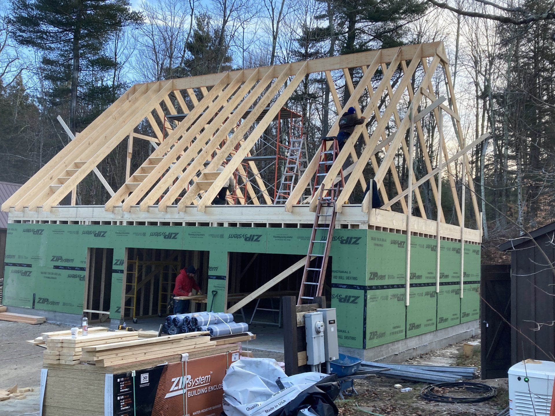 Wood-framed house under construction with green sheathing and workers on a roof ladder