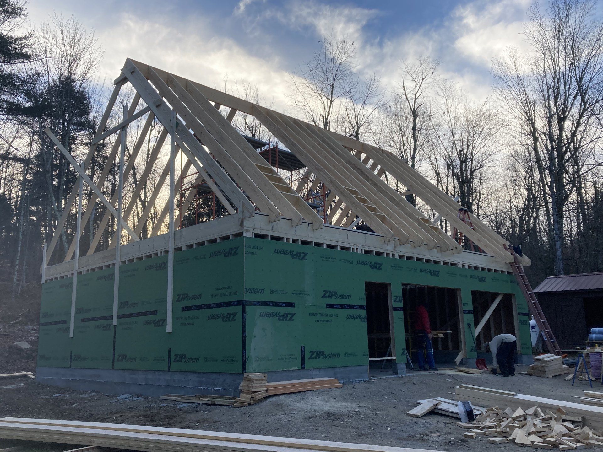 Partially framed house under construction with green sheathing and roof trusses in a snowy wooded area