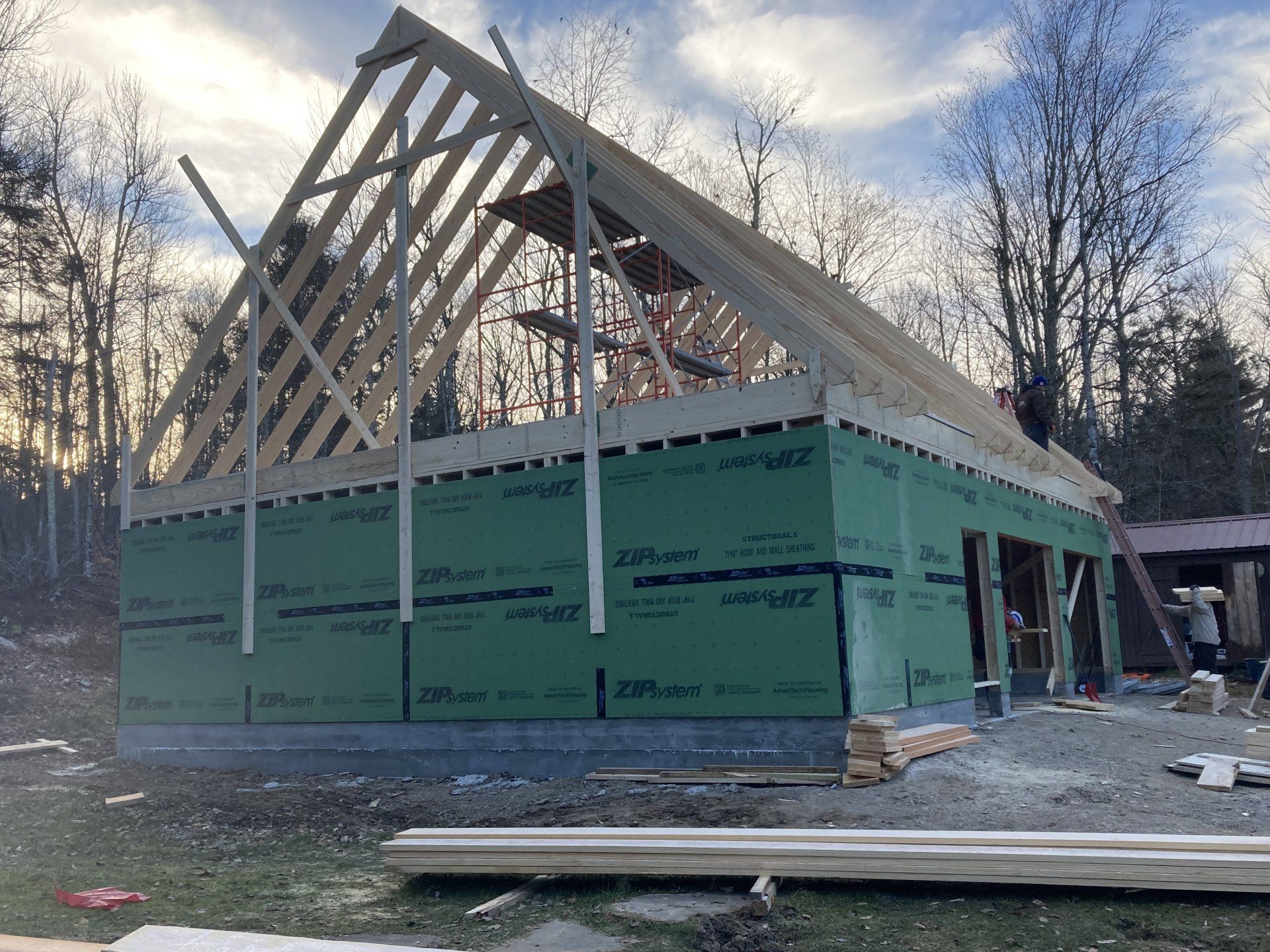 Partially built house with green sheathing and exposed roof framing at a wooded construction site